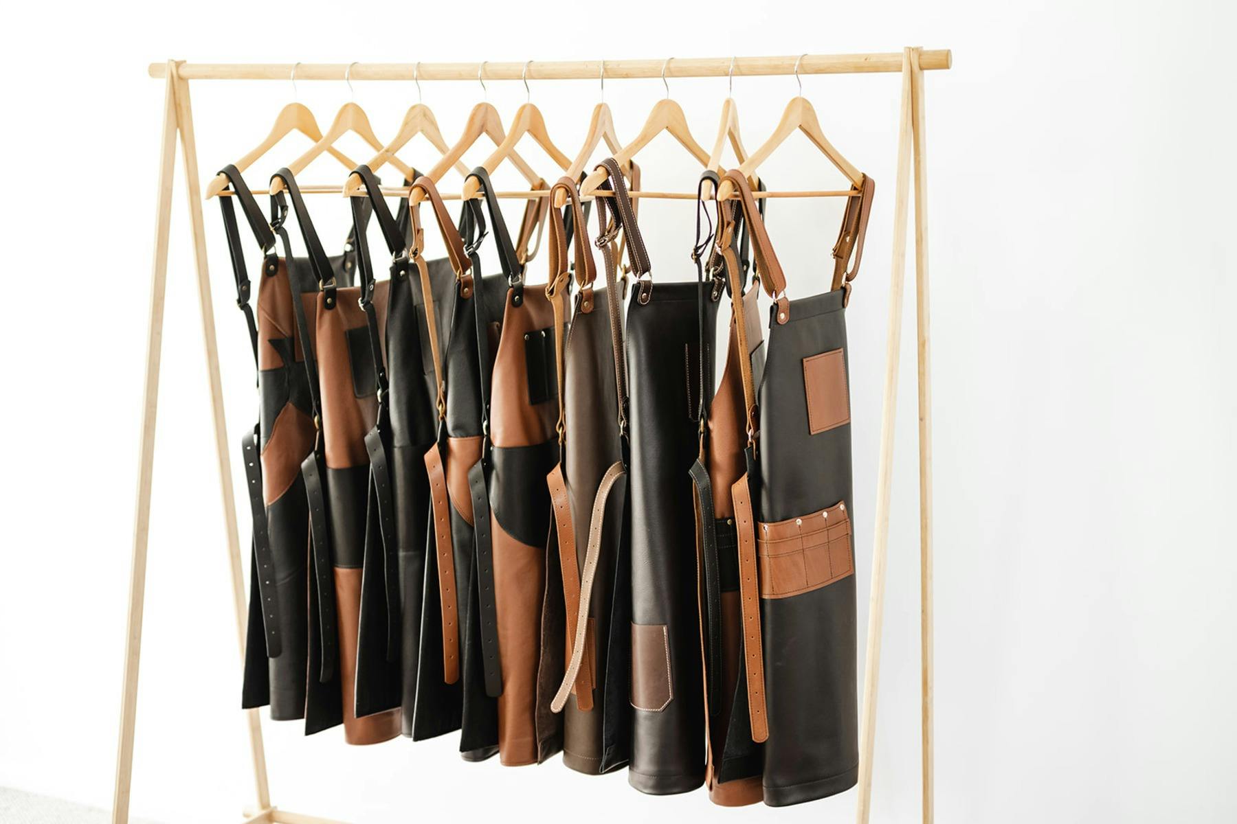 Handcrafted leather aprons in black and brown hanging on a wooden rack in a workshop