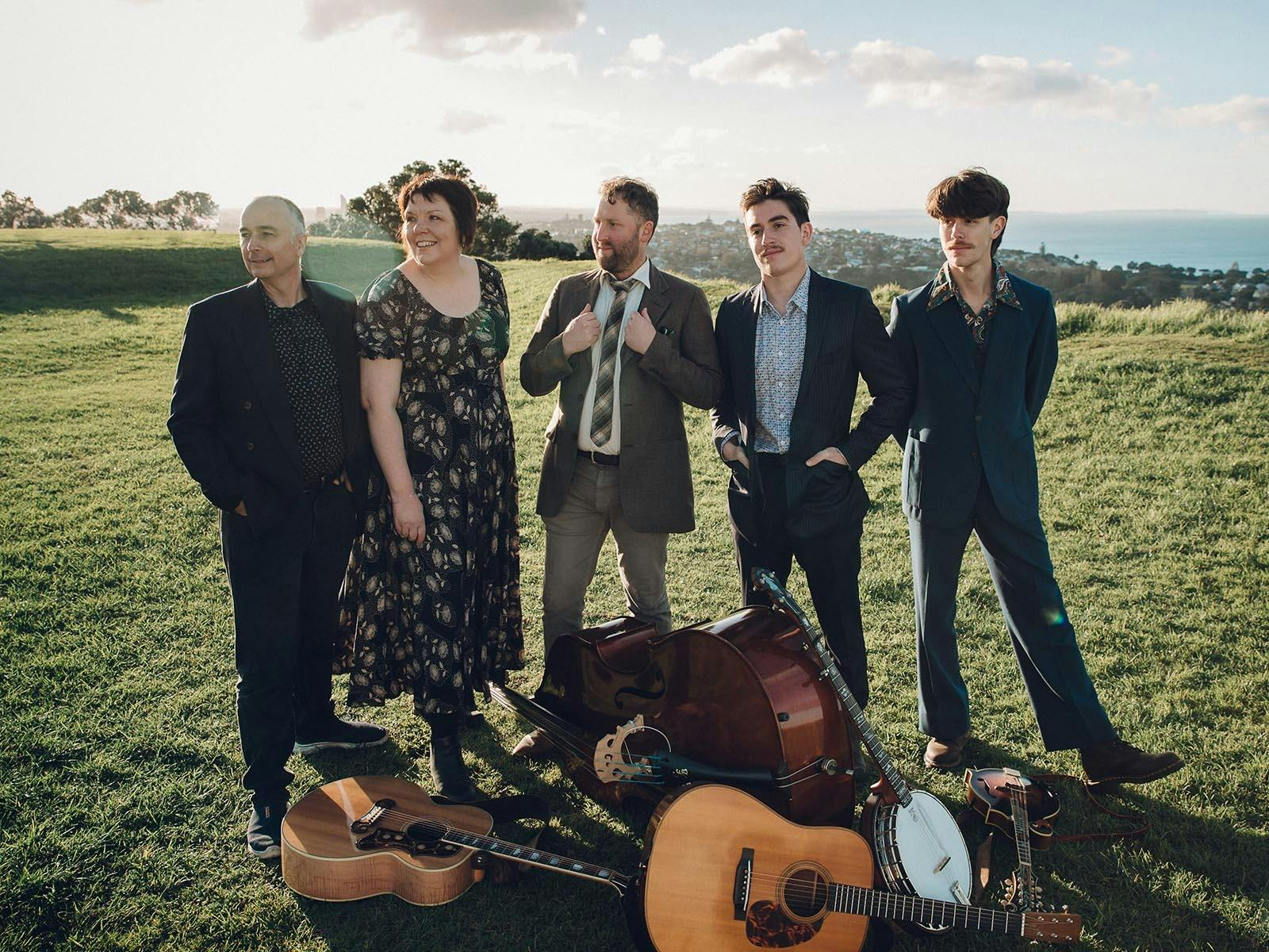 A group of musicians standing behind their instruments, incl a banjo, guitar, mandolin