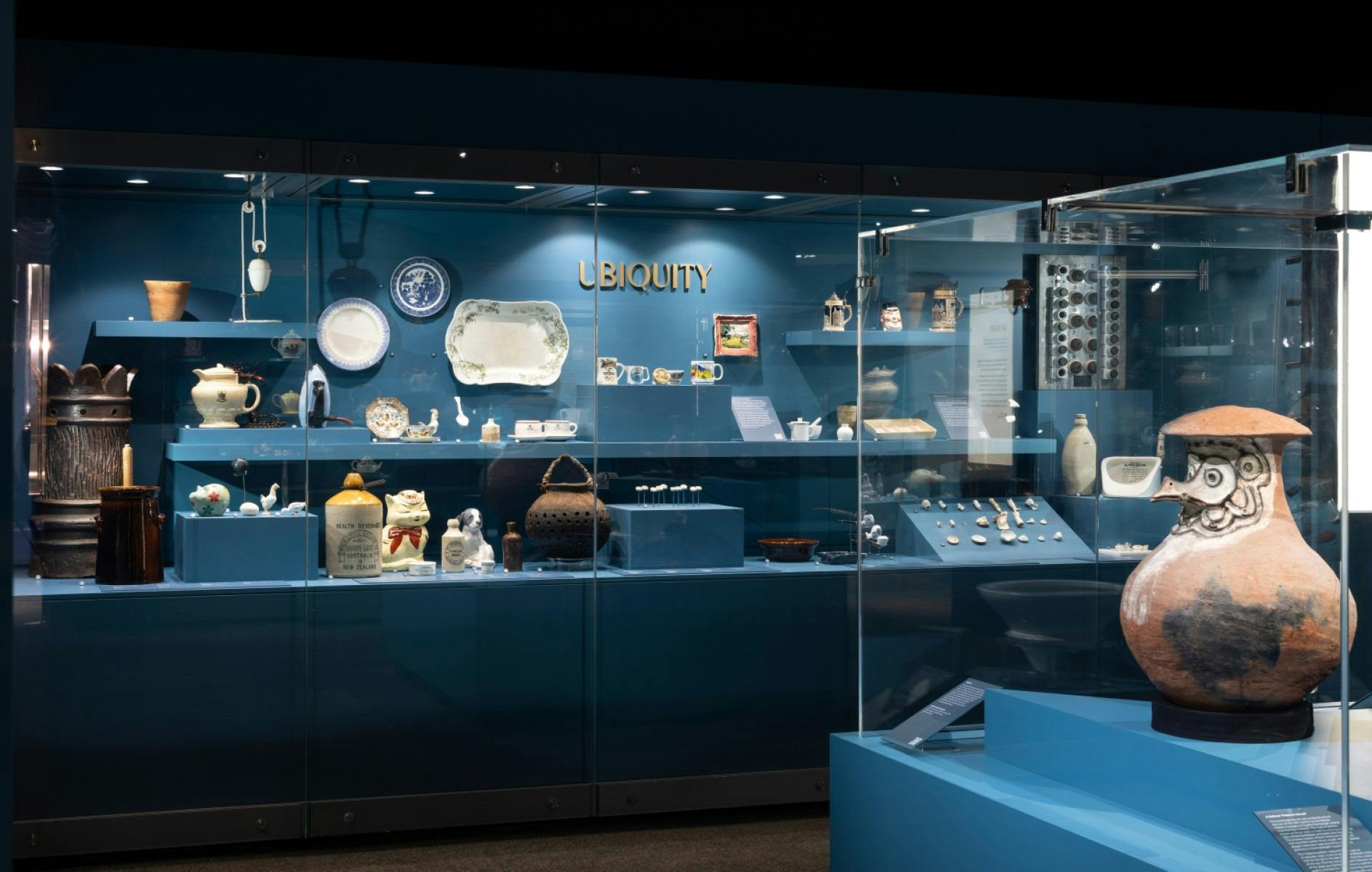 A small exhibition space lit with blue and glass showcases featuring many ceramic objects