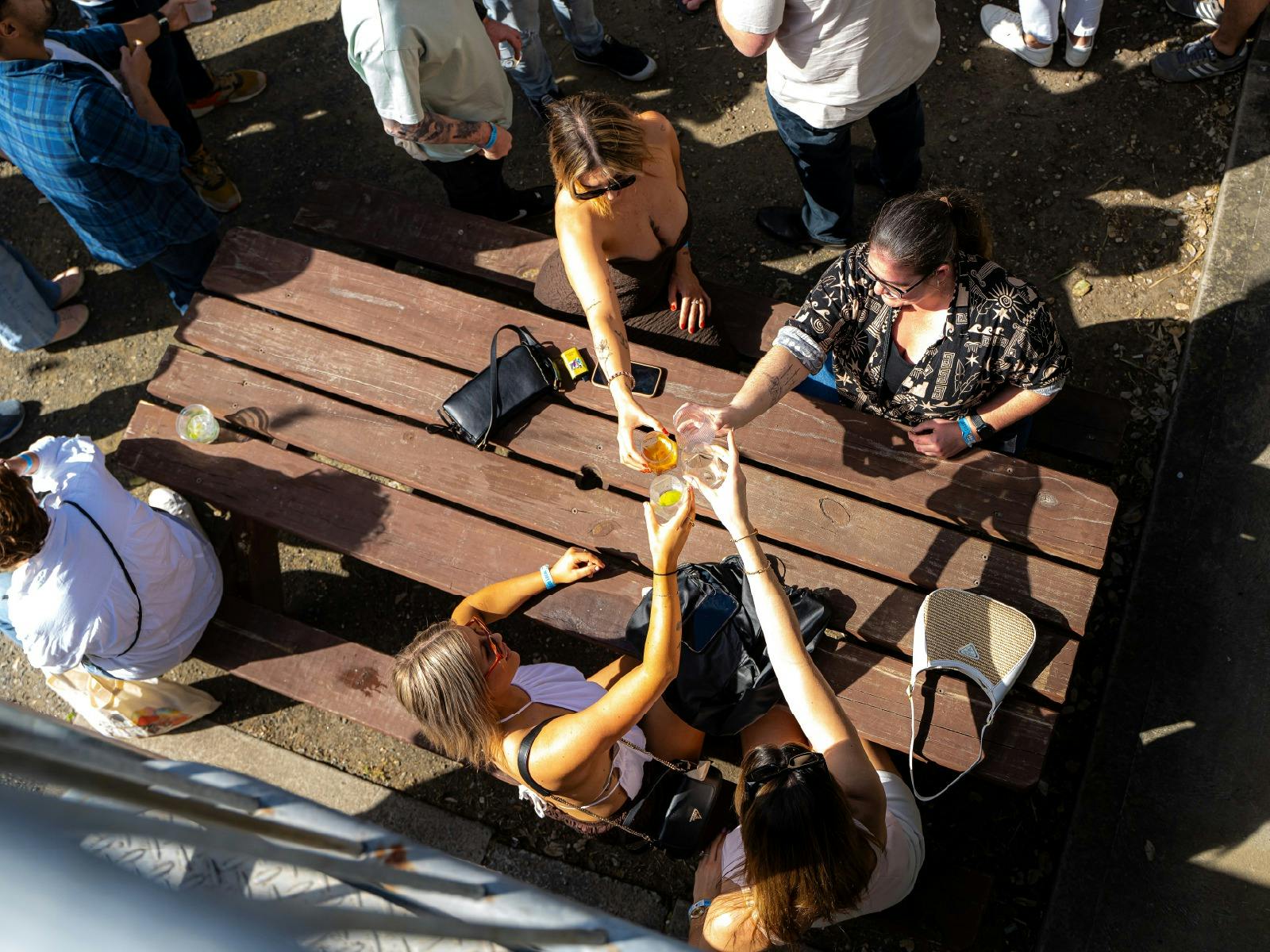 A group of four women cheers their glasses at an outdoor table during Pours 2025