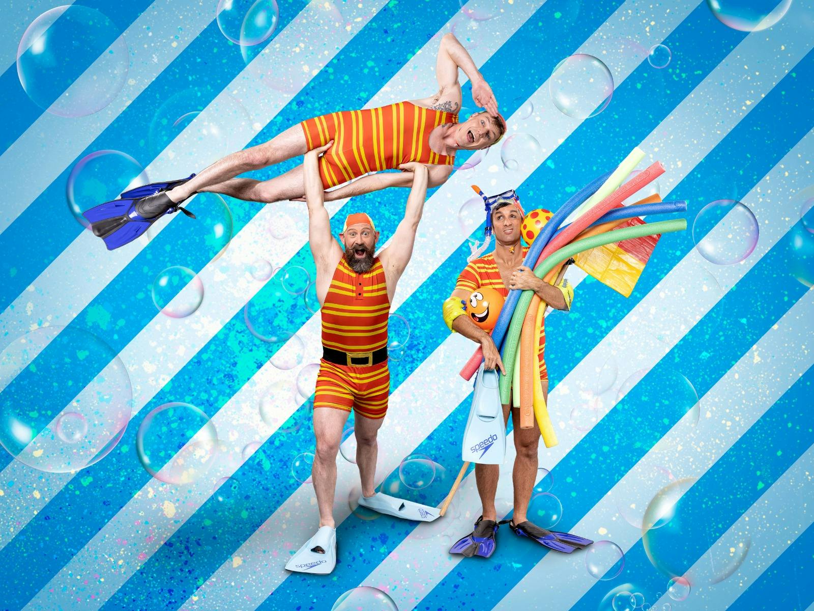 Three men in bathing outfits strike acrobatic poses against a blue backdrop