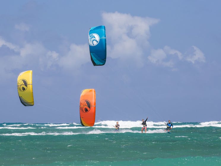 3 kiteboarders all surfing in towards beach
