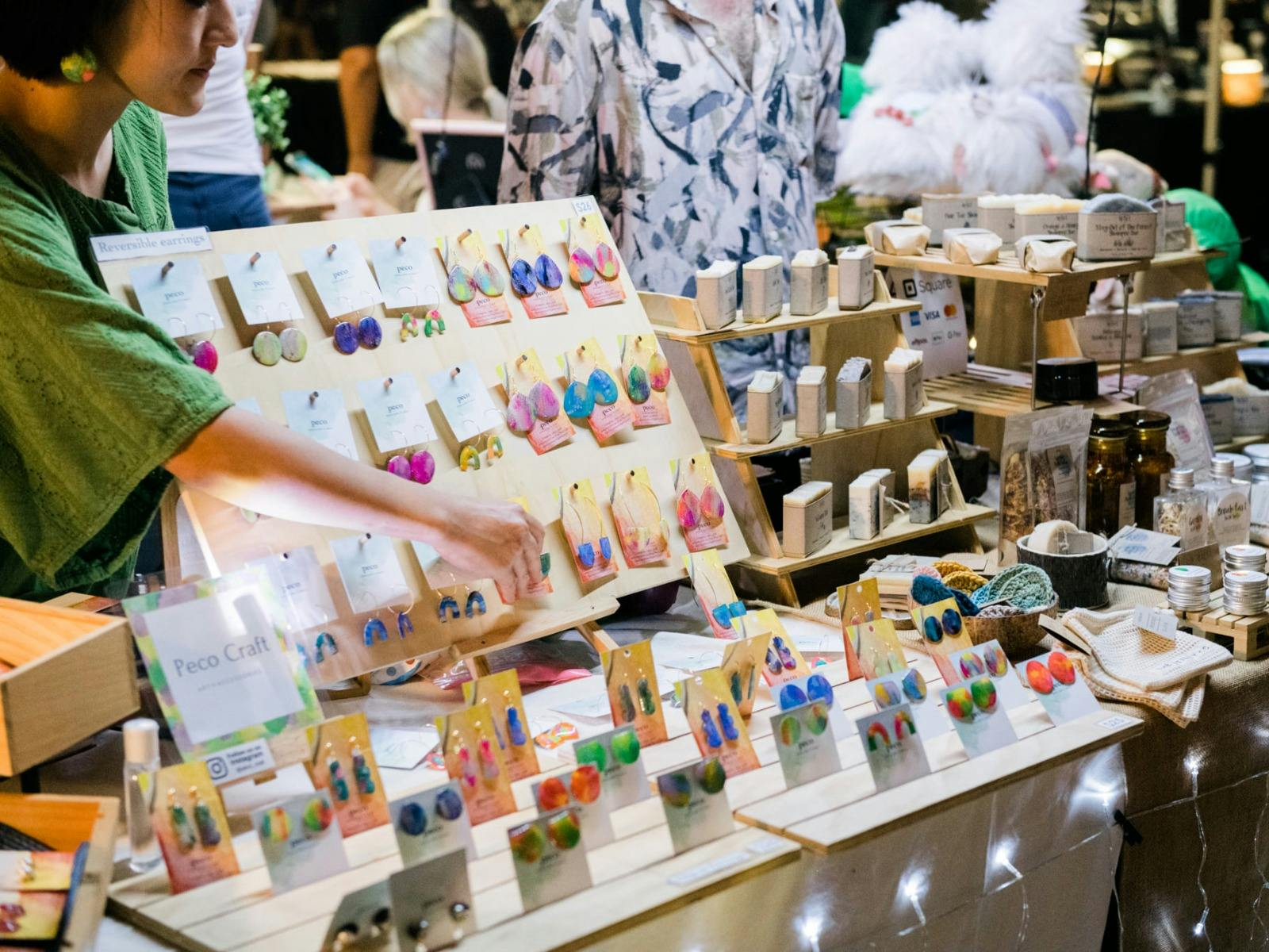 A close up of a jewellery stand at night with a woman reaching across it