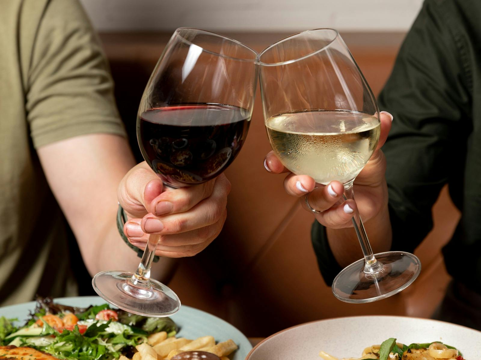 Two people's arms doing a cheers motion with their wine. Food down the bottom of the image.