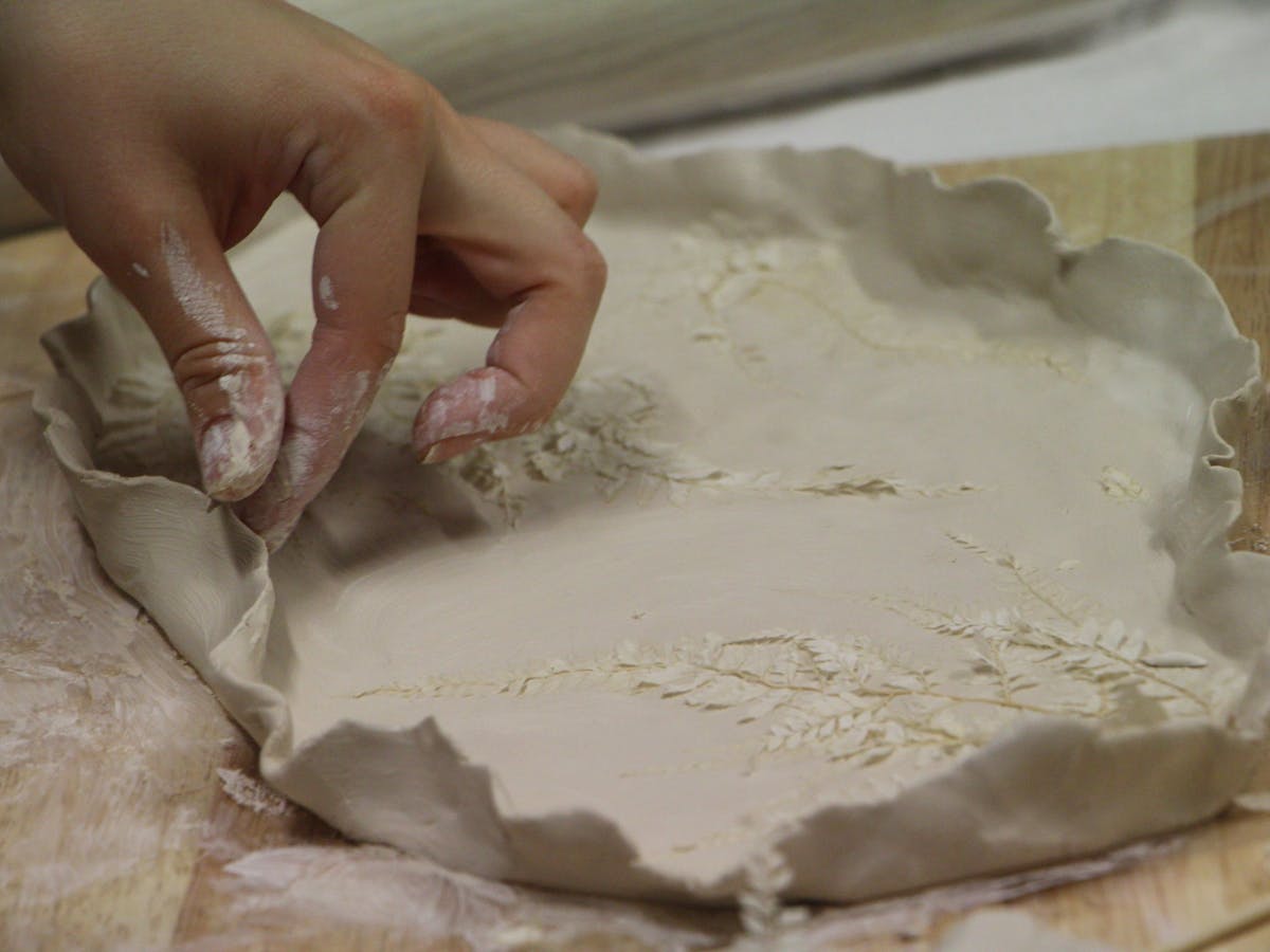 Hand shaping clay slab with pressed botanical textures on wooden board