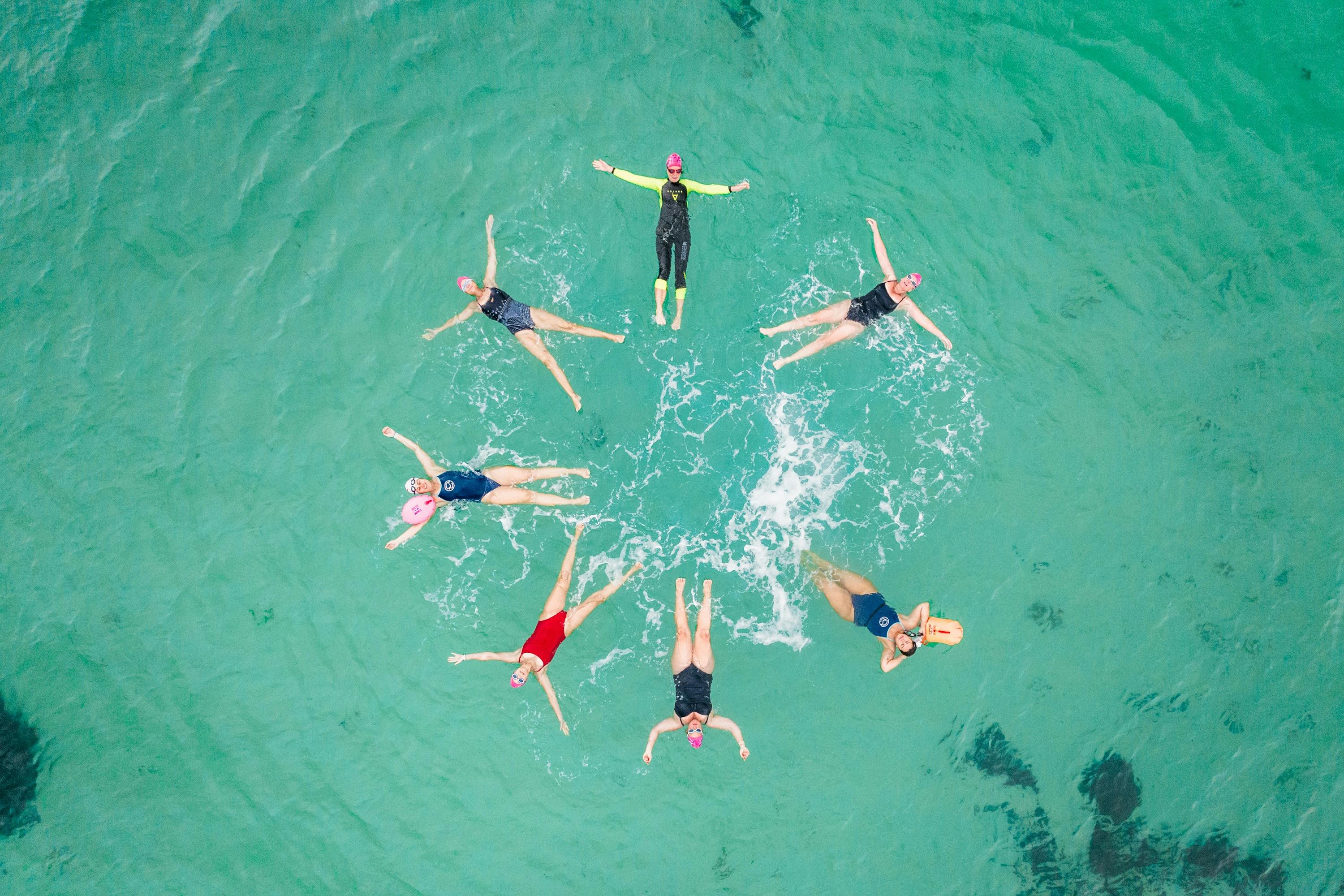 7 people float in a circle formation viewed from above, in the ocean