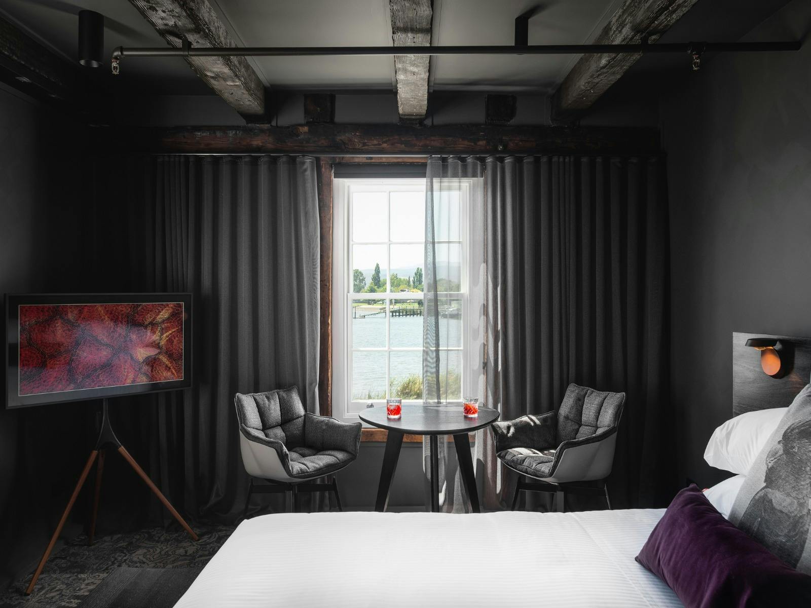 A king bed with a stylish table and chair by the window