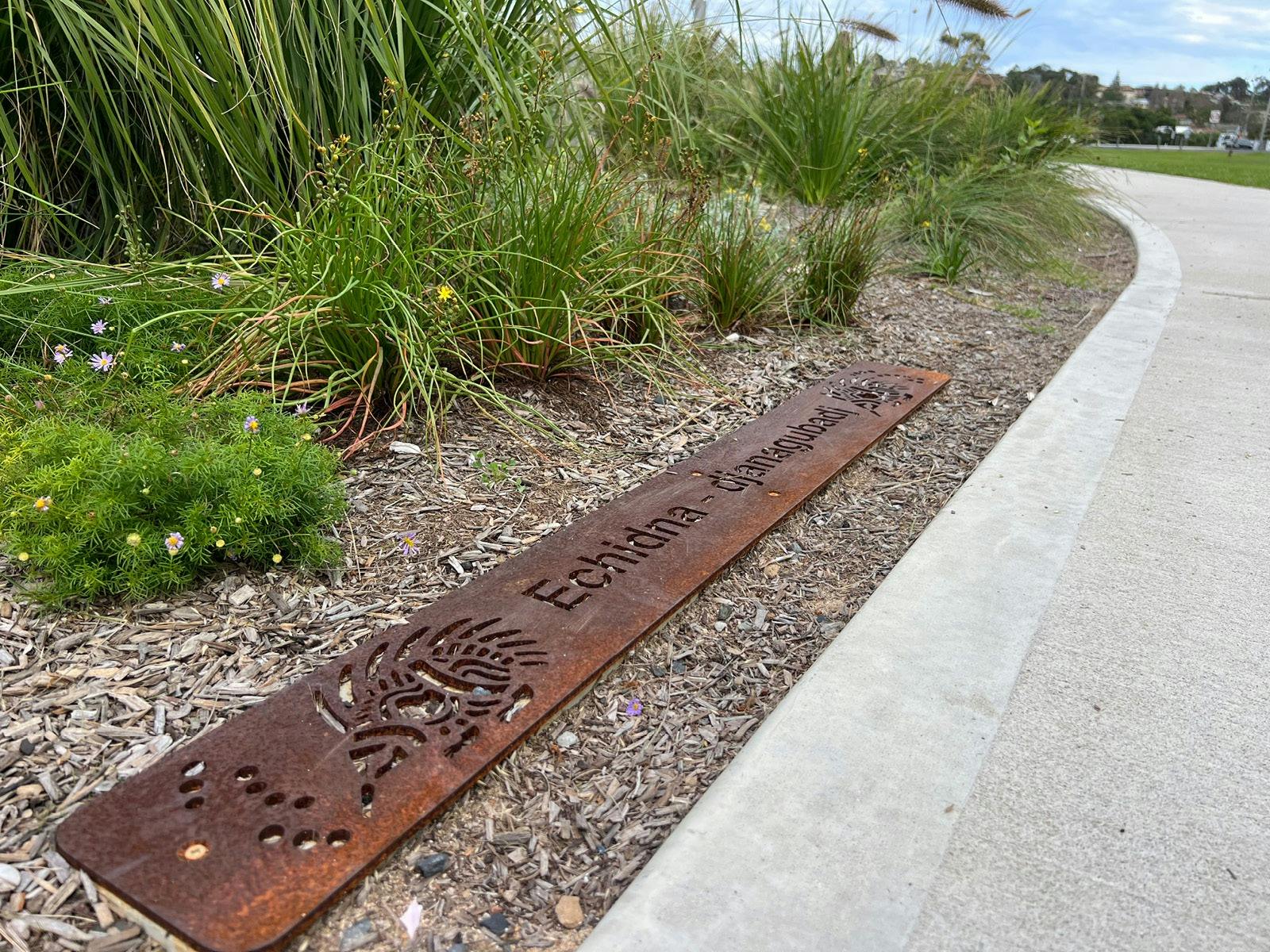 a rusted steel plate with words cut out and located next to a concrete path