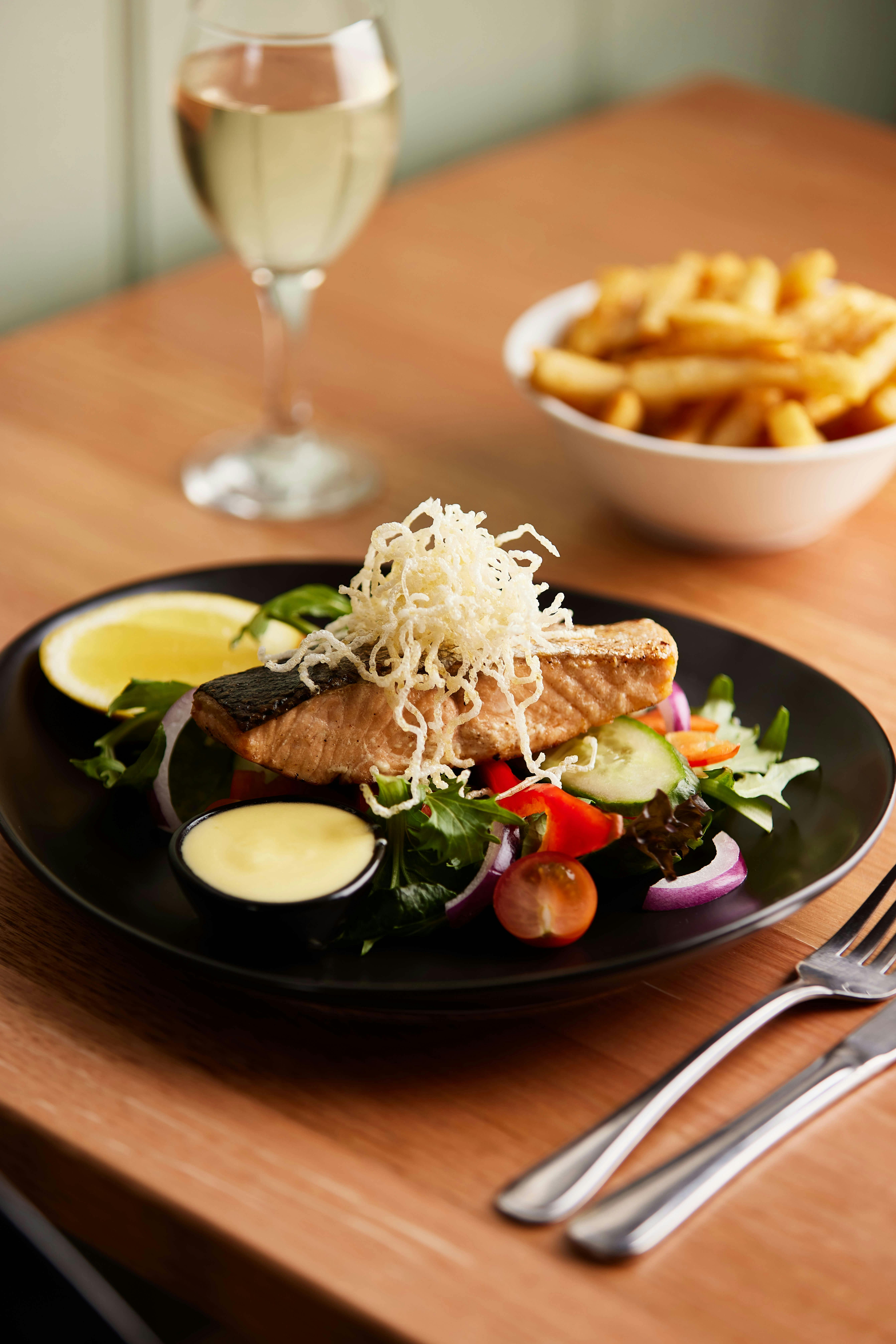 A fish meal on a plate with salad and a bowl of chips in the background