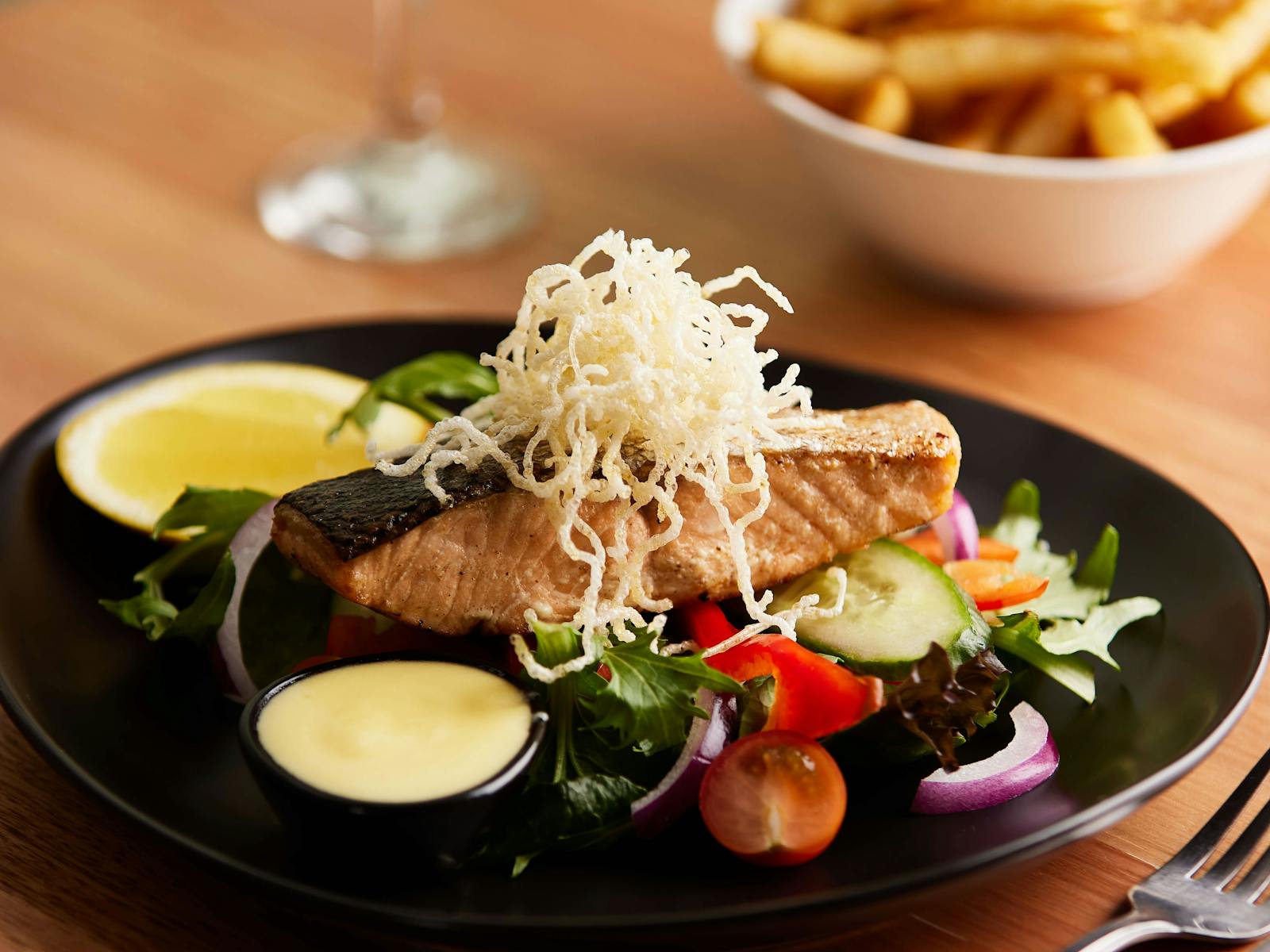 A fish meal on a plate with salad and a bowl of chips in the background