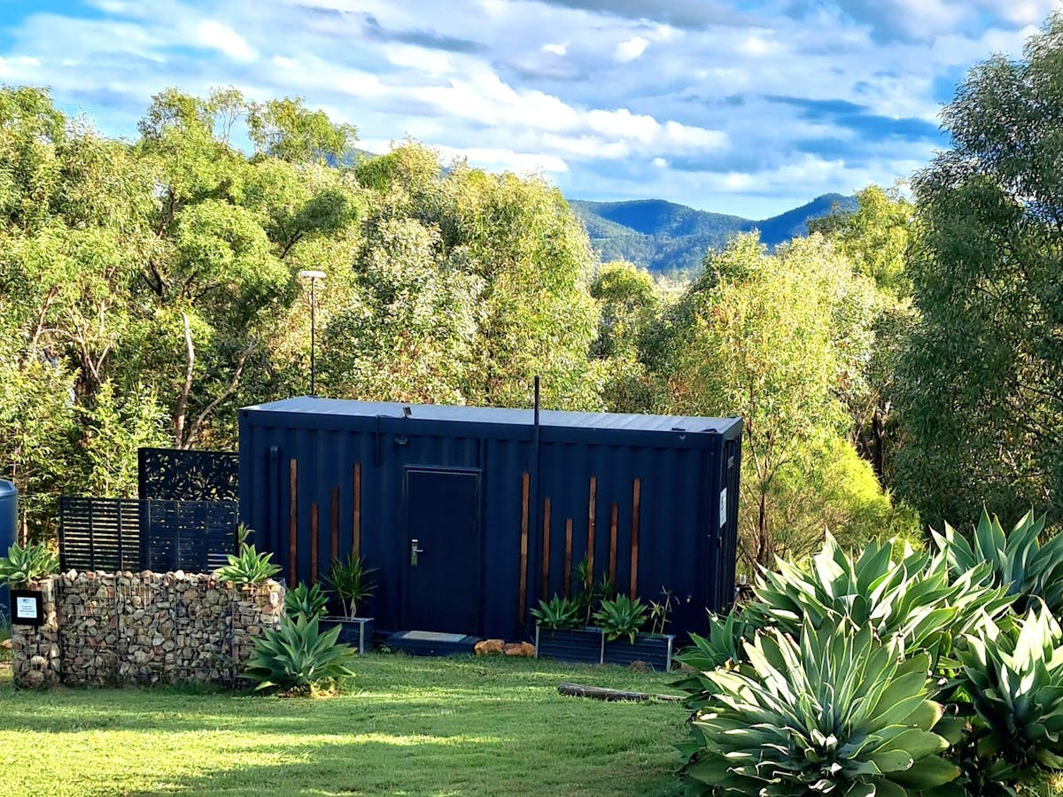 a black container converted into a tiny home with a green bush setting and mountains beyond a black container converted into a tiny home with a green bush setting and mountains beyond