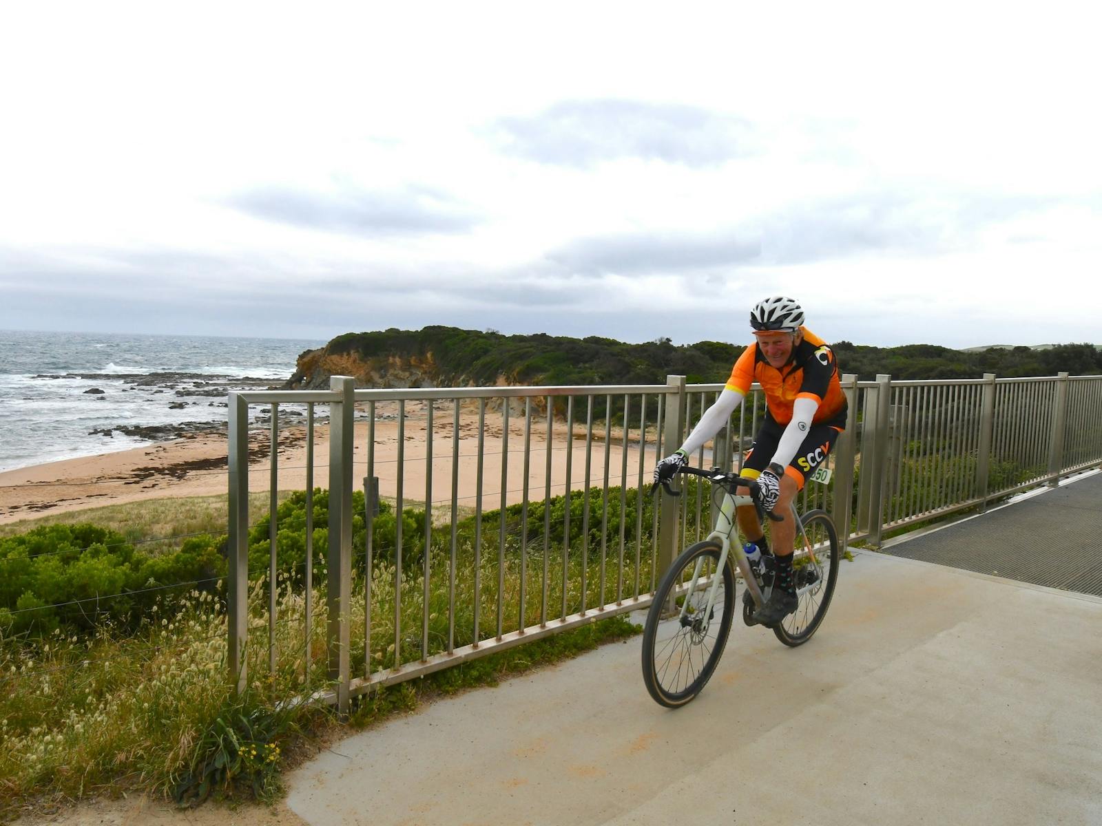 Cyclist on a bridge with ocean and cliff in background