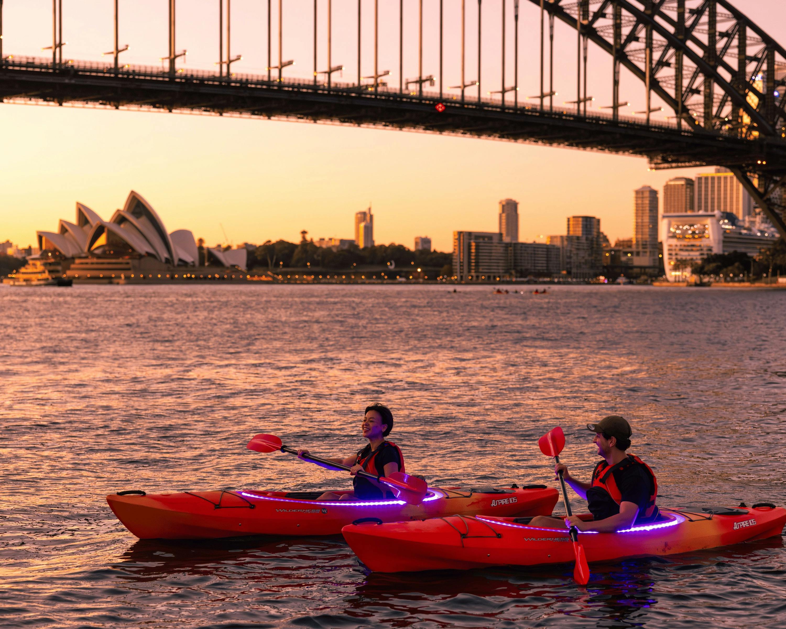 日出时分，两个人划着桨在悉尼海港大桥旁游弋。