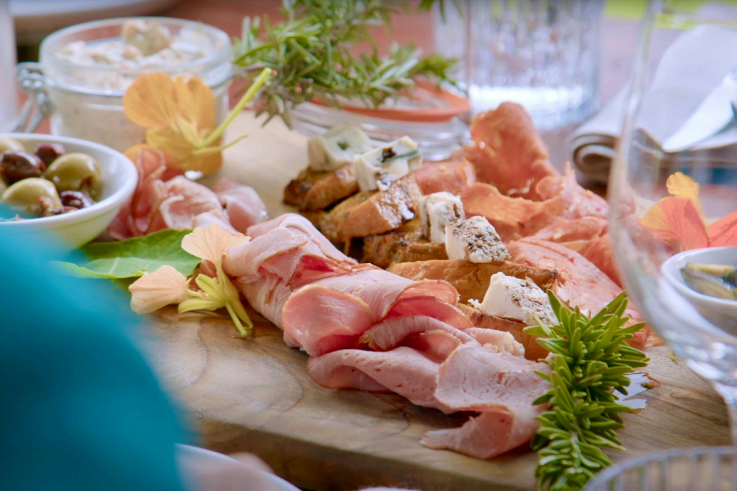 A platter of cold meats, cheese, dips, bread and olives on a wooden board