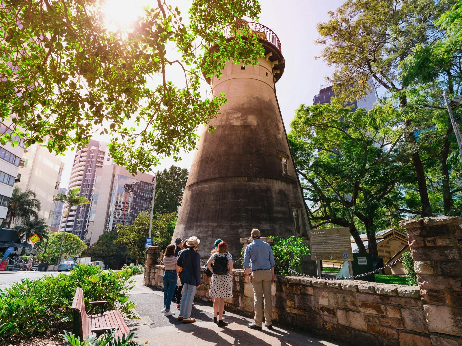 A group of people on a walking tour stand in front of a large windmill.
