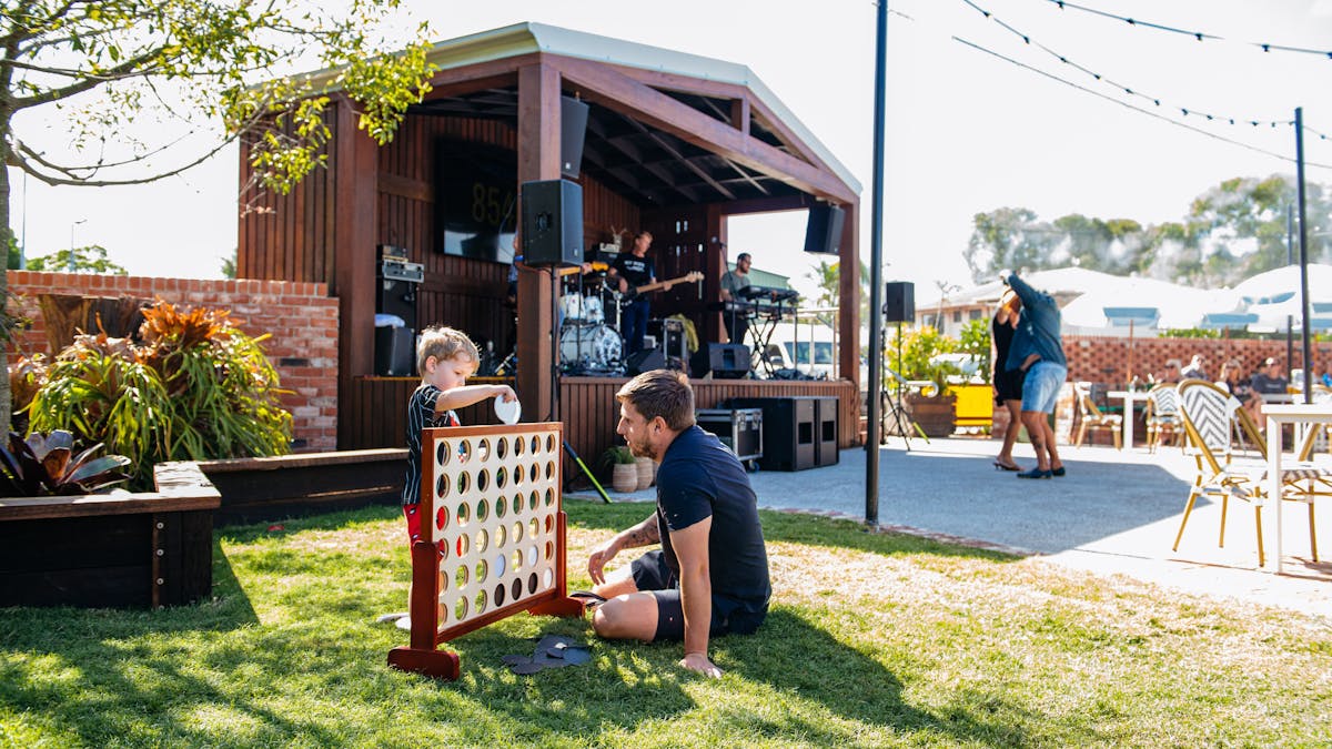 A young boy and a man play a game on a sunny lawn while a live band performs on stage