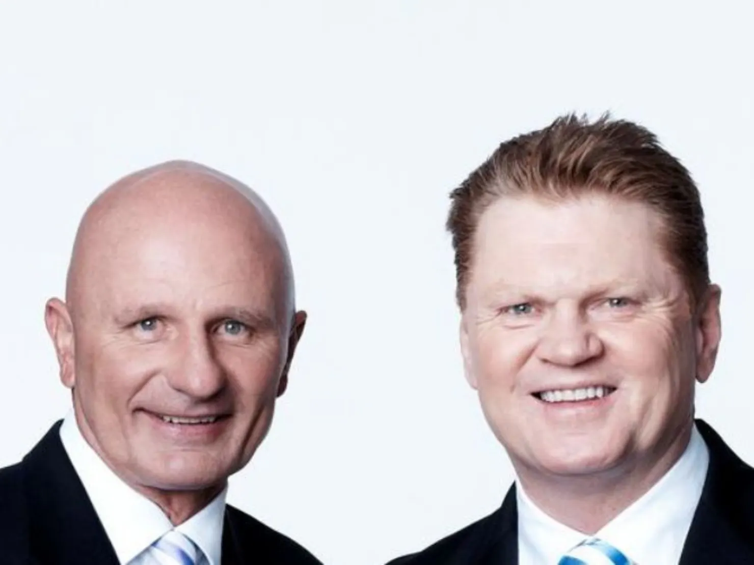 Two middle aged man in black suit against a white background.