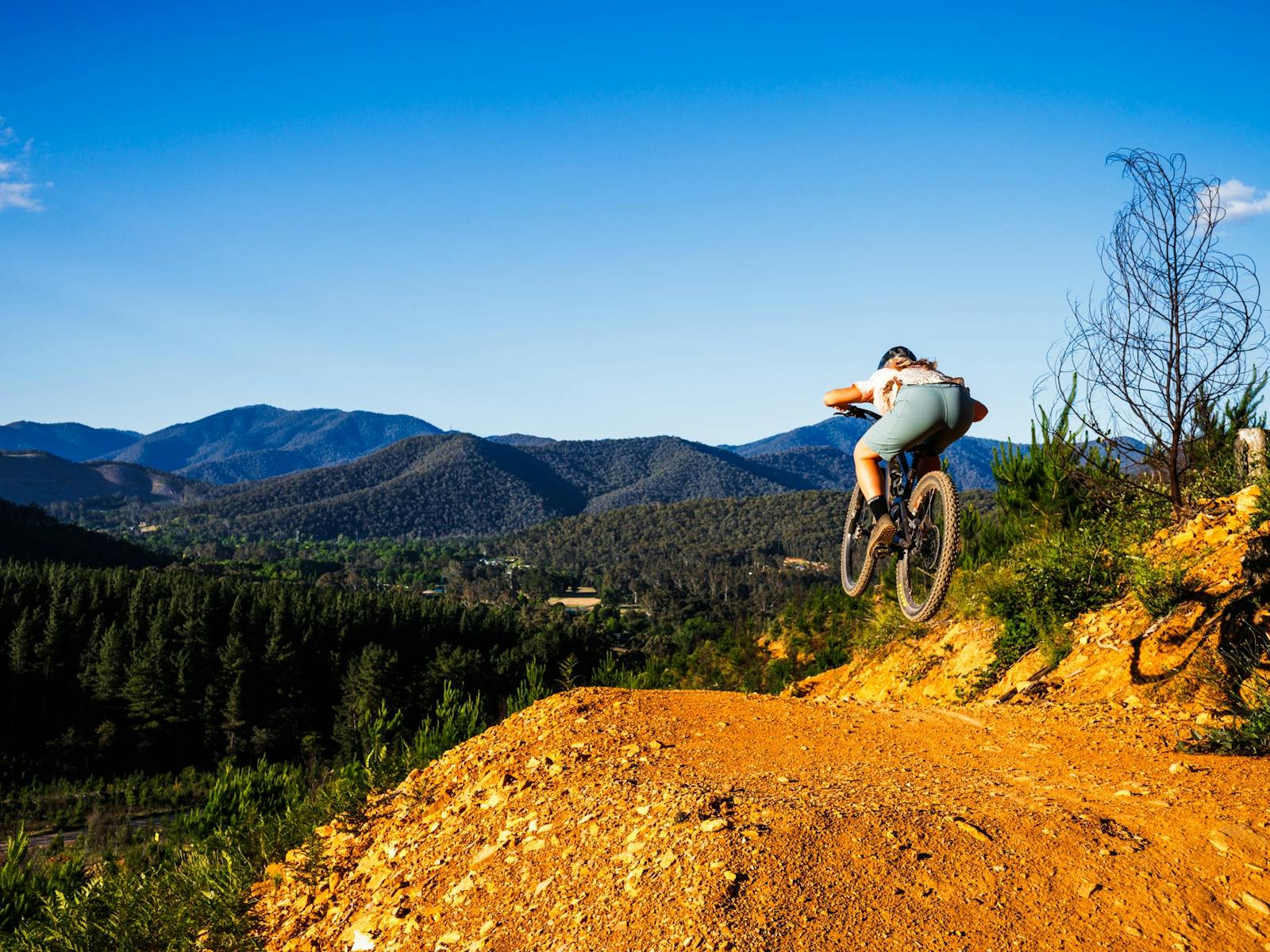 MTB riders doing a jump with mtb bike with mountains in the backdrop
