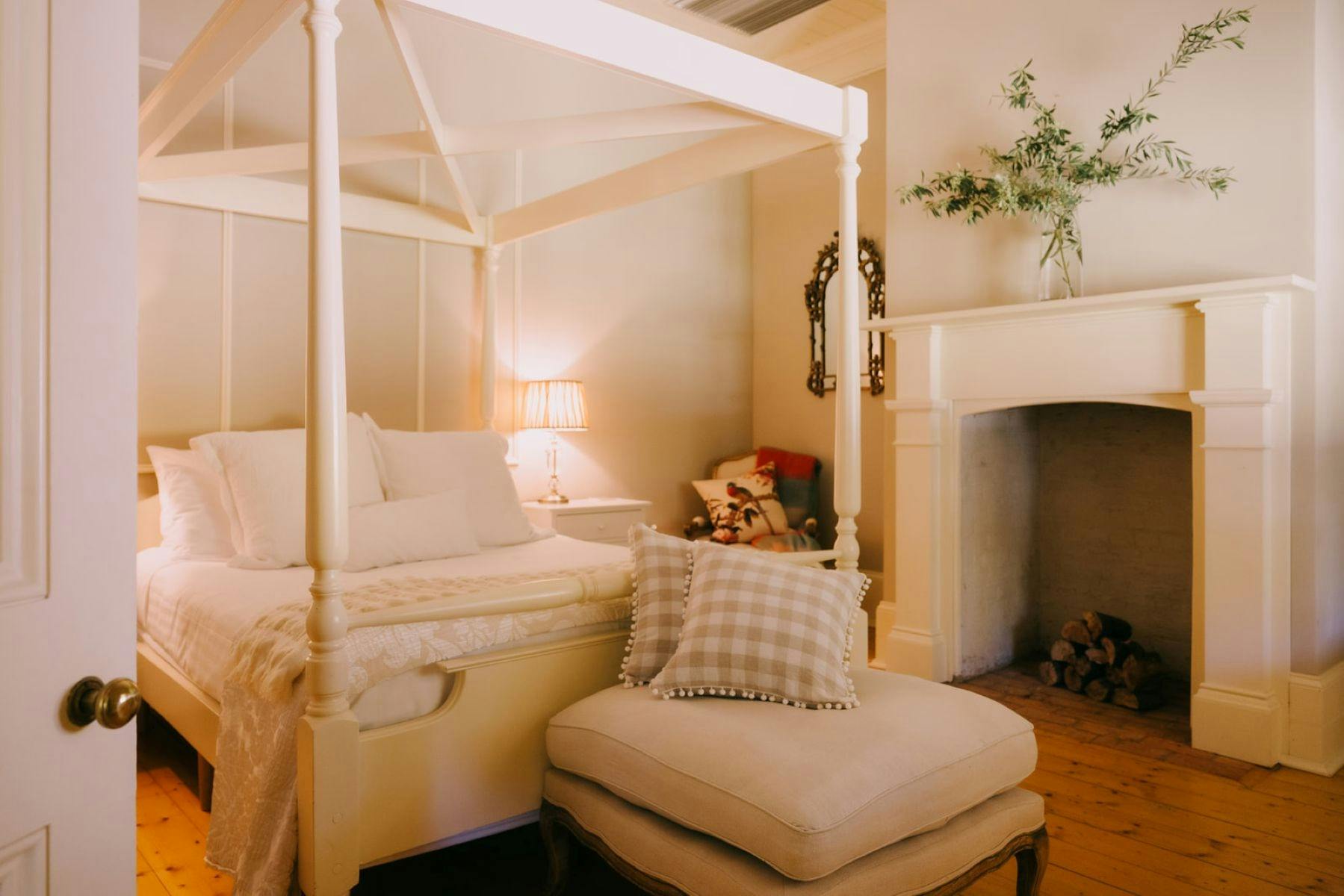 A cozy bedroom featuring a four-poster bed, an ottoman and a warming fireplace.