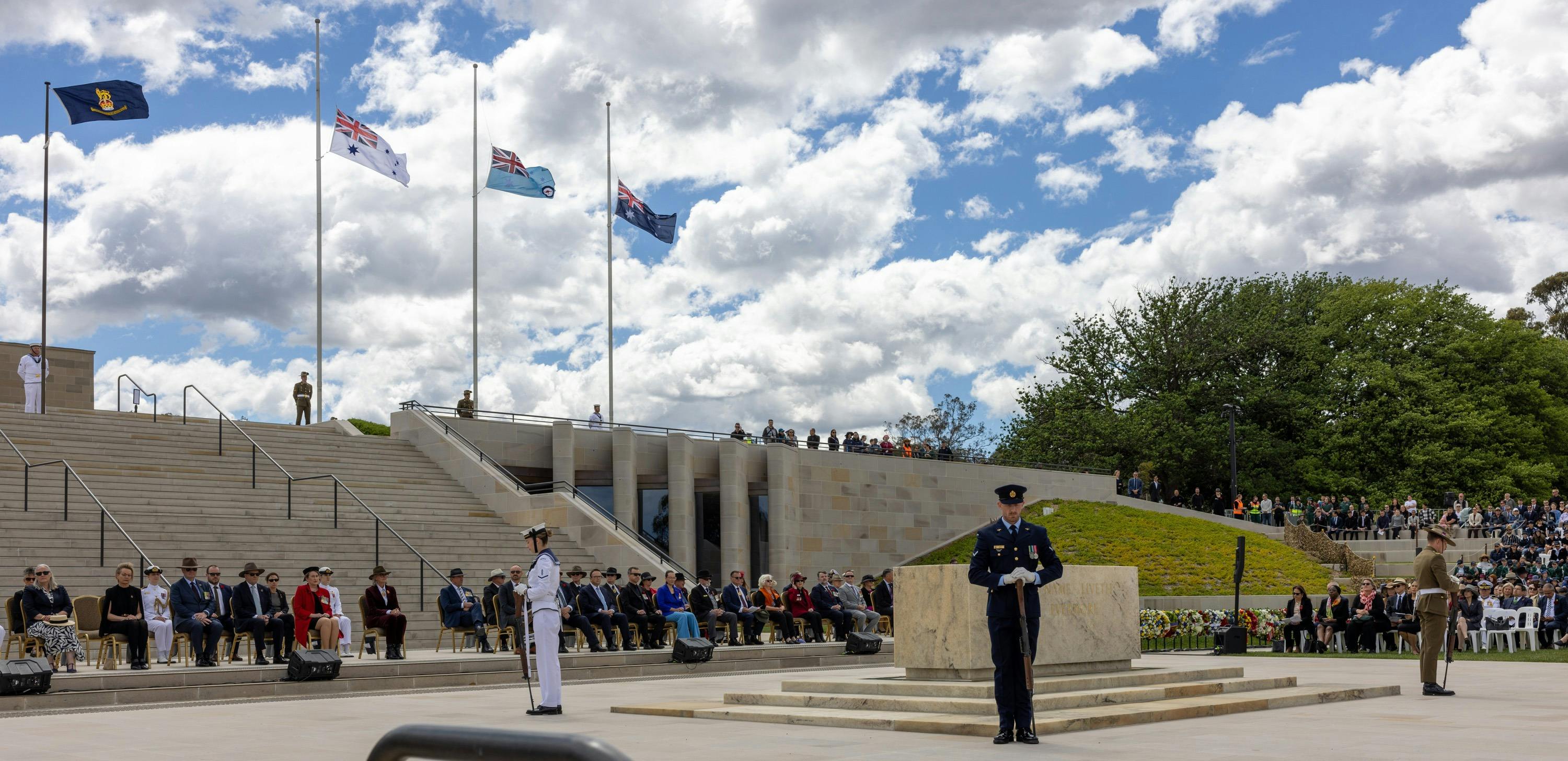 Flags at half mast, stone of remembrance and soldiers standing at each corner