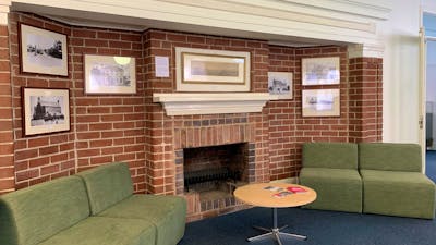 Image of a red brick fire place with historic photo display and green chairs