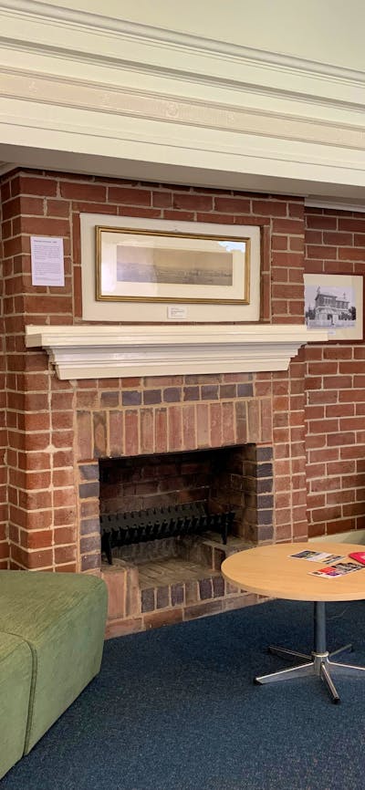 Image of a red brick fire place with historic photo display and green chairs