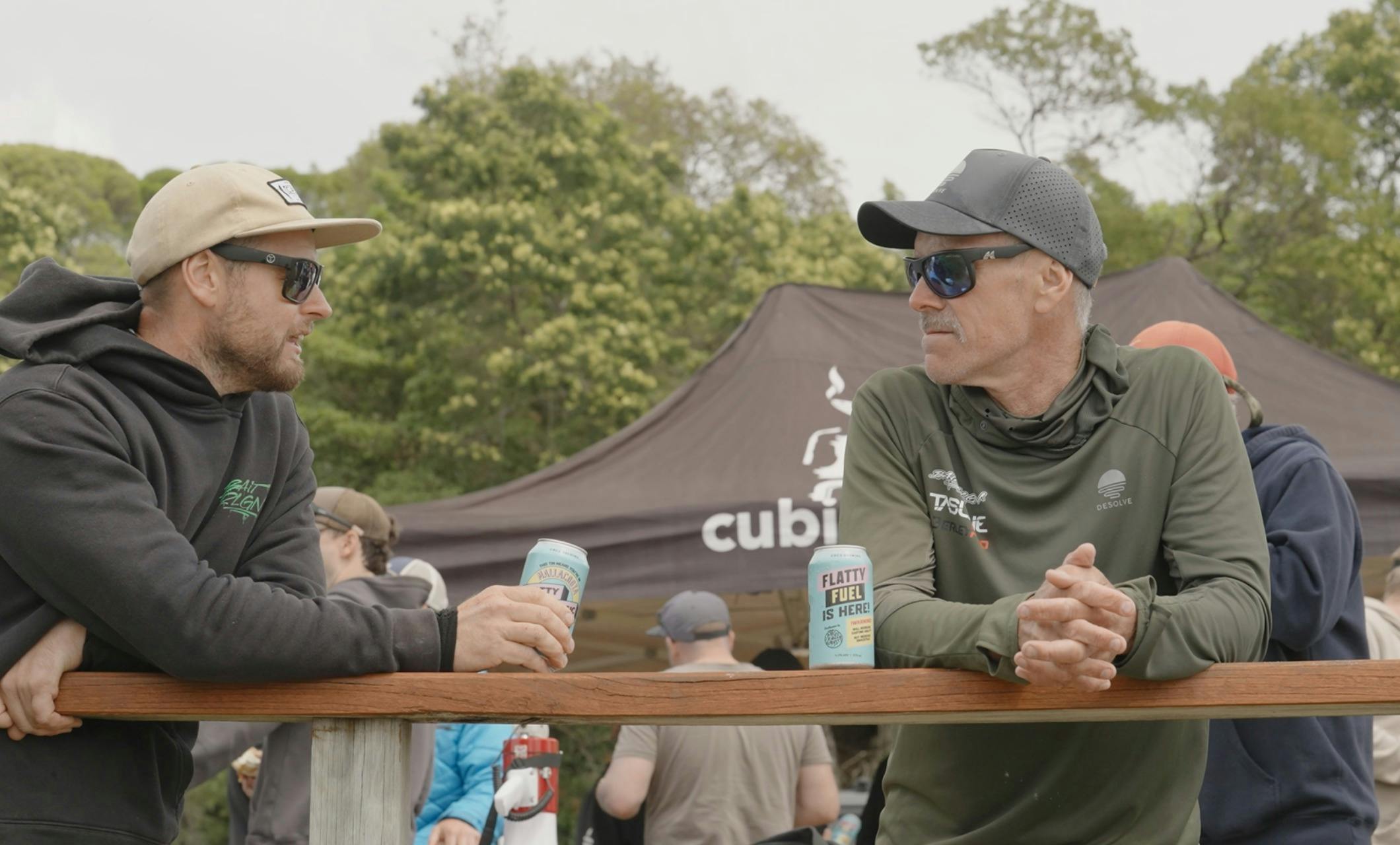Two anglers lean on a timber rail chatting at the event marquee