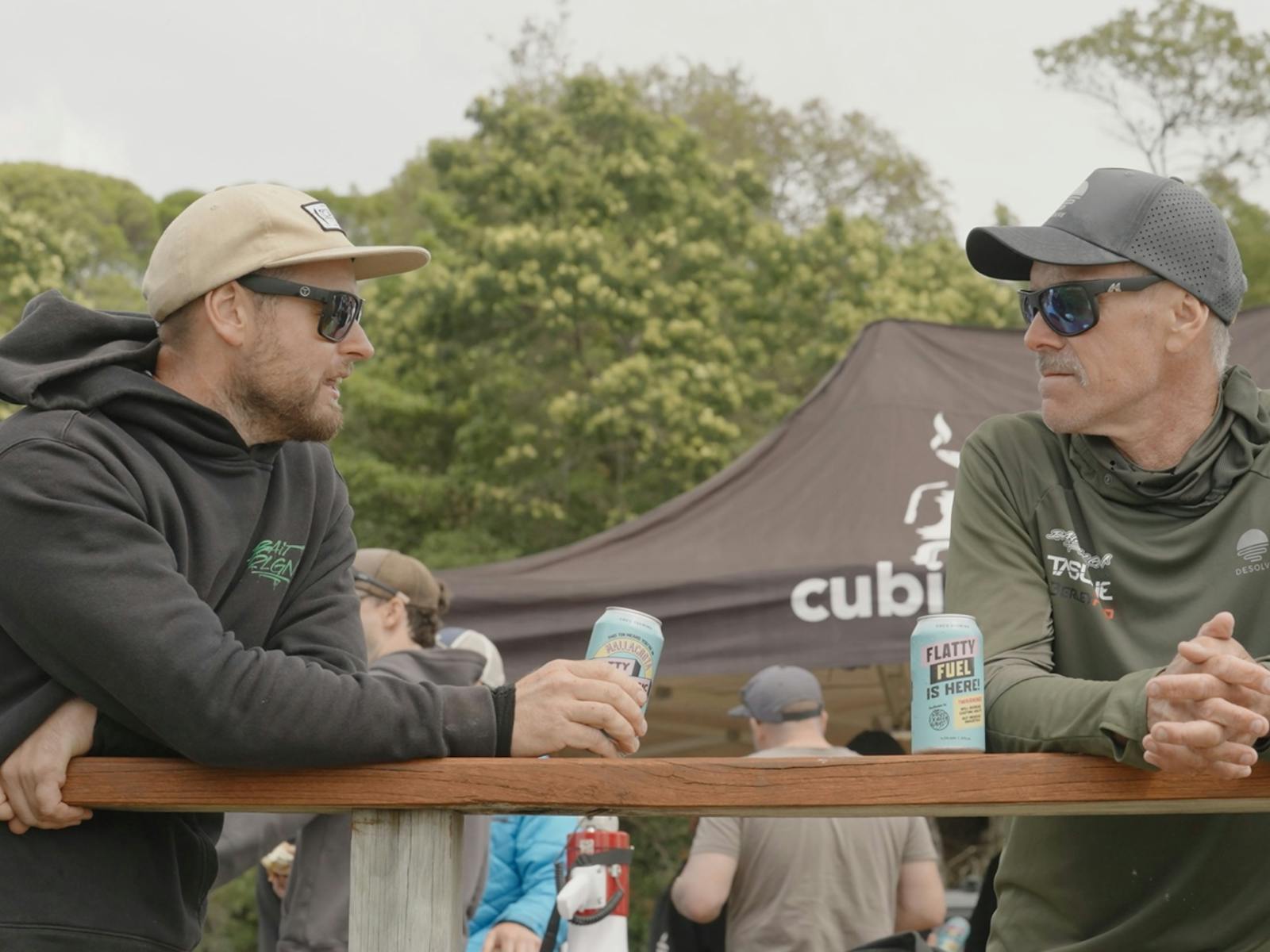 Two anglers lean on a timber rail chatting at the event marquee