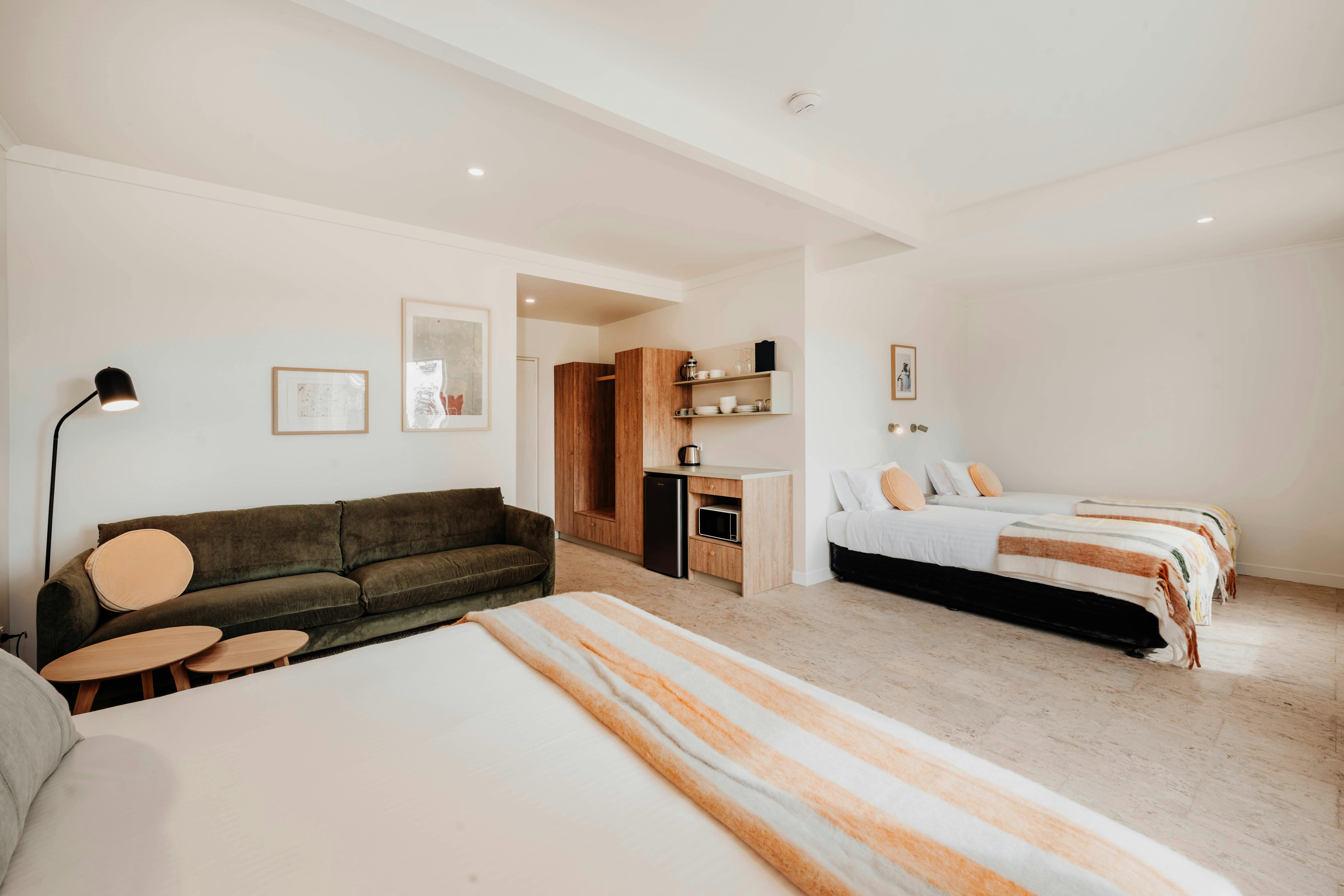 Motel room with green sofa, queen bed and two king single beds, each crisp white sheets