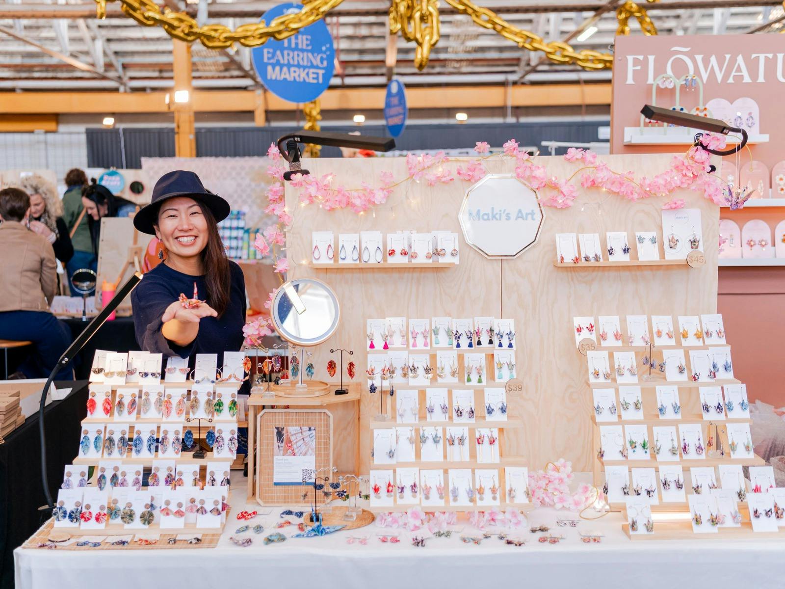 A Stallholders stands behind her stall holding out oragami in her hand