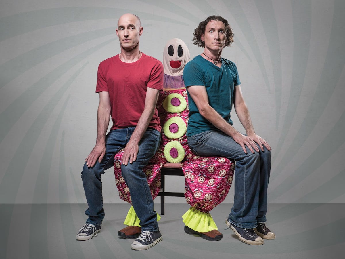 Umbilical Brothers sitting on the lap of a clown called Roadie, looking uncomfortable