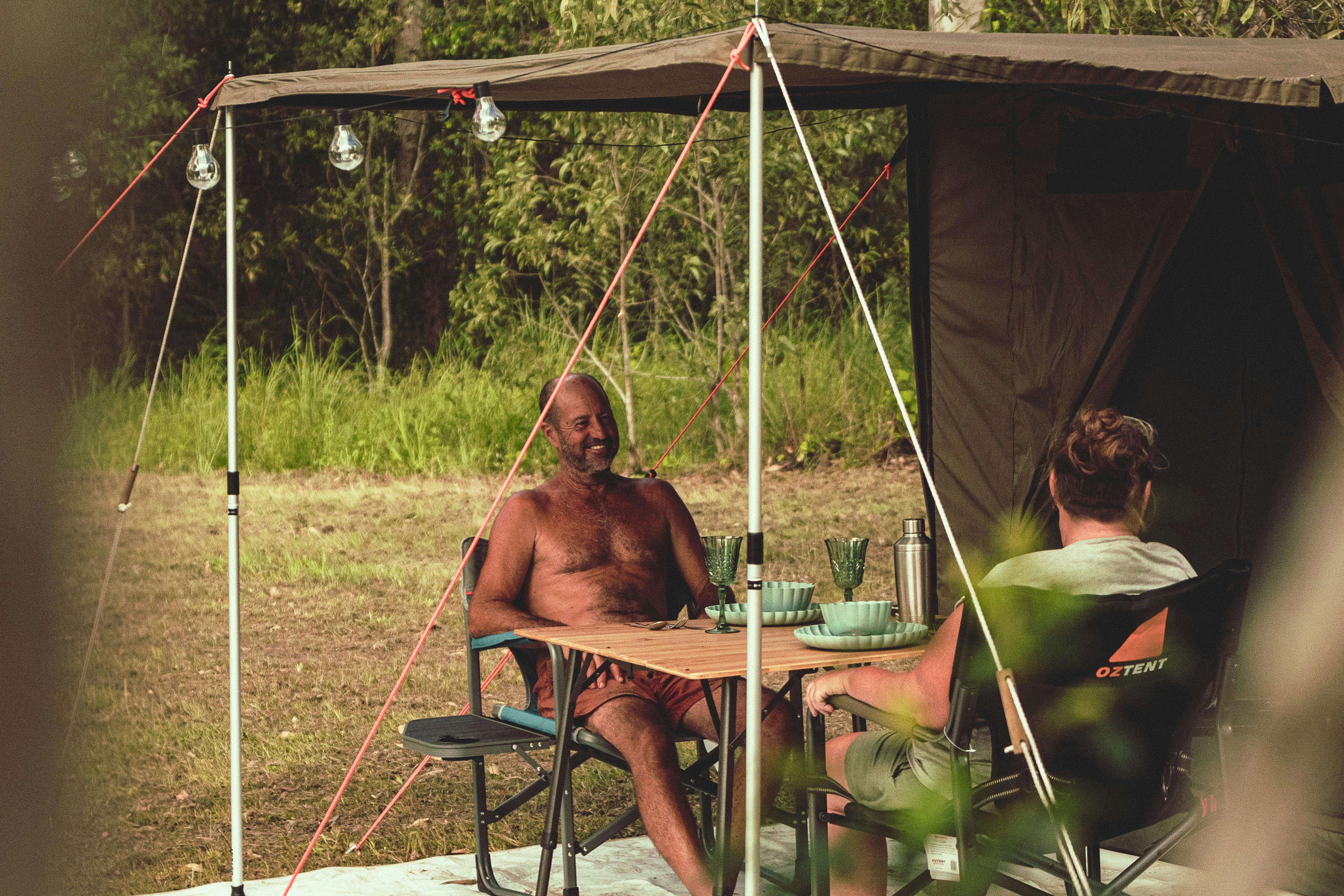 two people chatting at a table under the awning of a safari tent