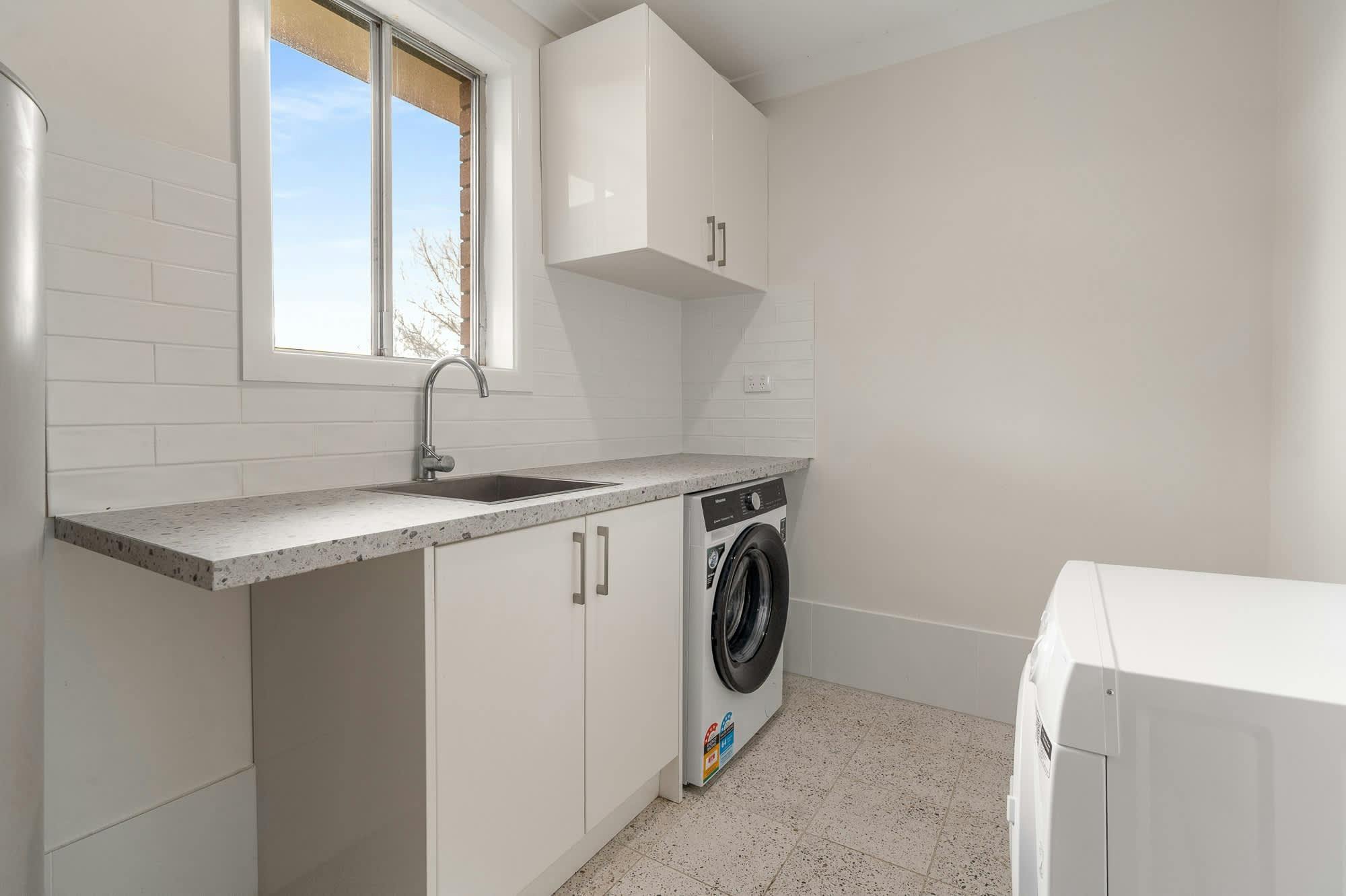 Bright white laundry with a large sink, storage, washing machine & dryer