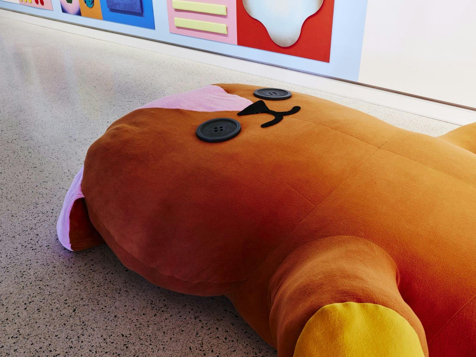 giant teddy bear lying on the ground next to colourful wall