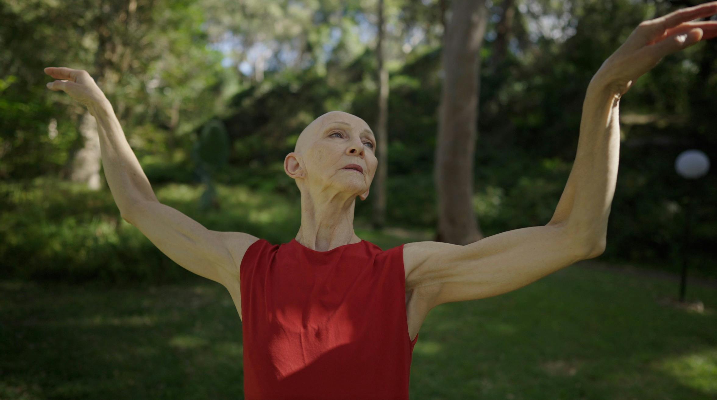 Bald woman wearing red dress with bare arms held high