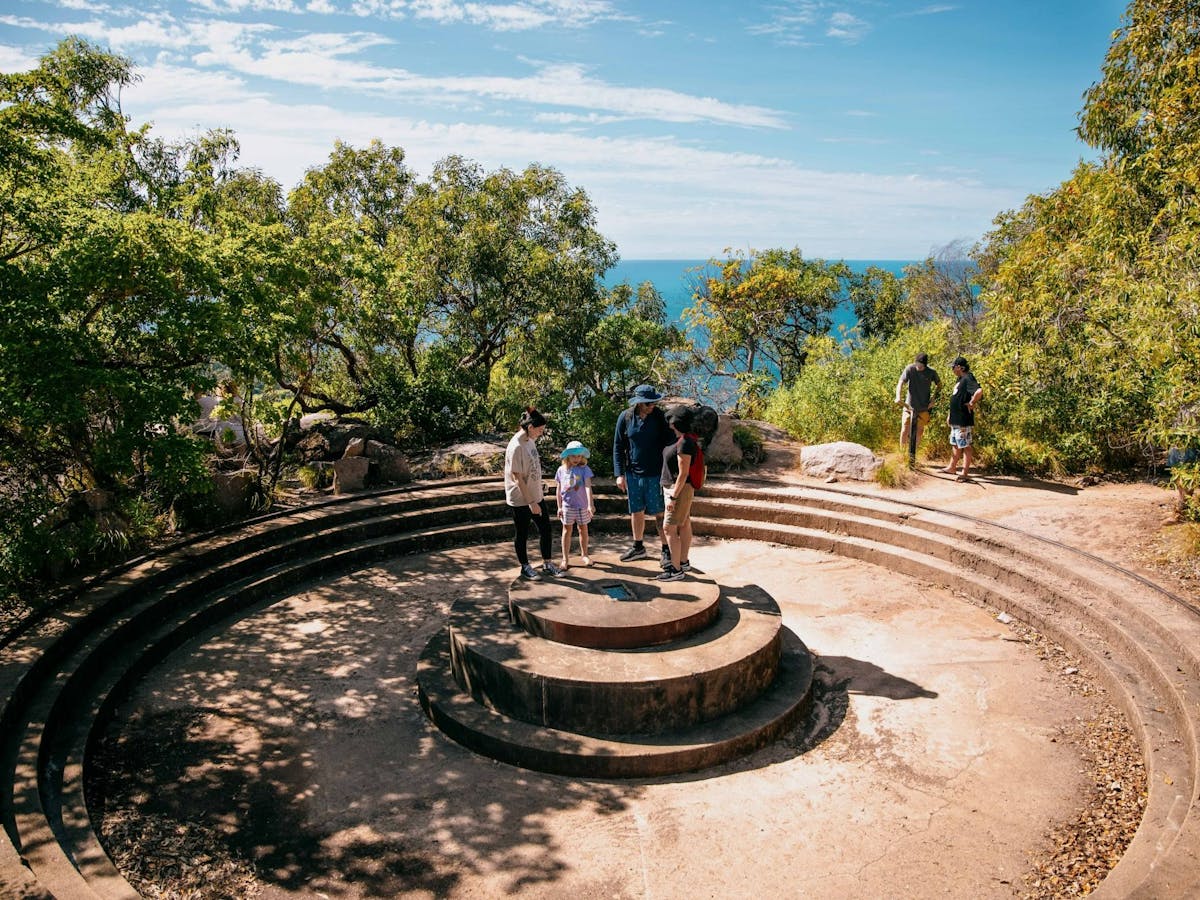 Round concrete gun emplacement with four people standing on it and another couple in background.