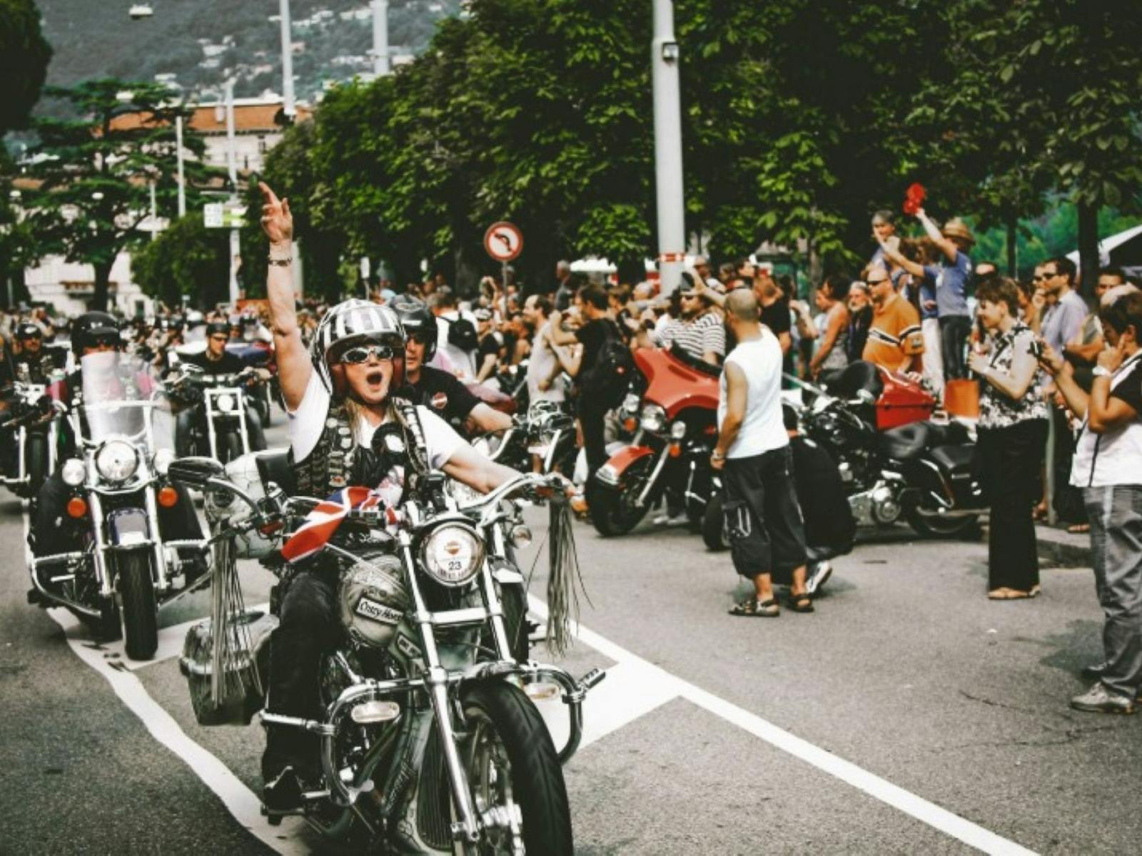 Bikers group along a road with a crowd cheering