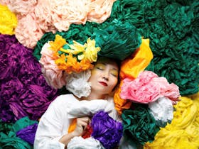 Artist Hiromi Tango lying down in amongst colourful paper flowers