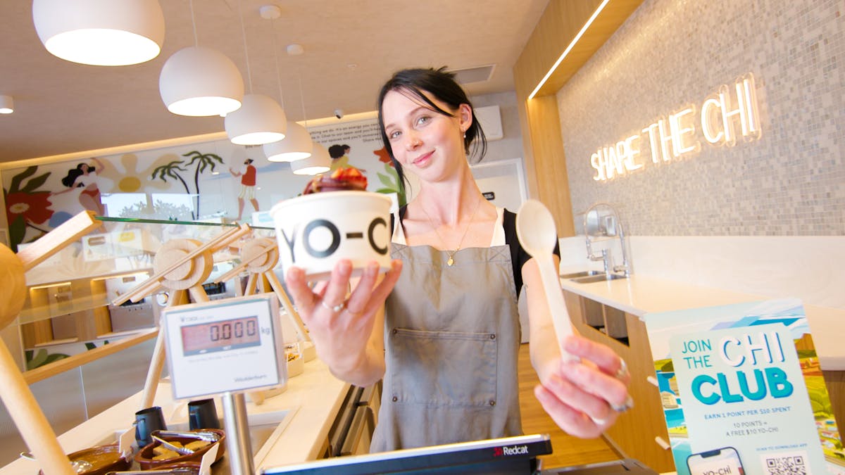 Yo-Chi worker holding a frozen yoghurt cup and spoon at Soul Boardwalk