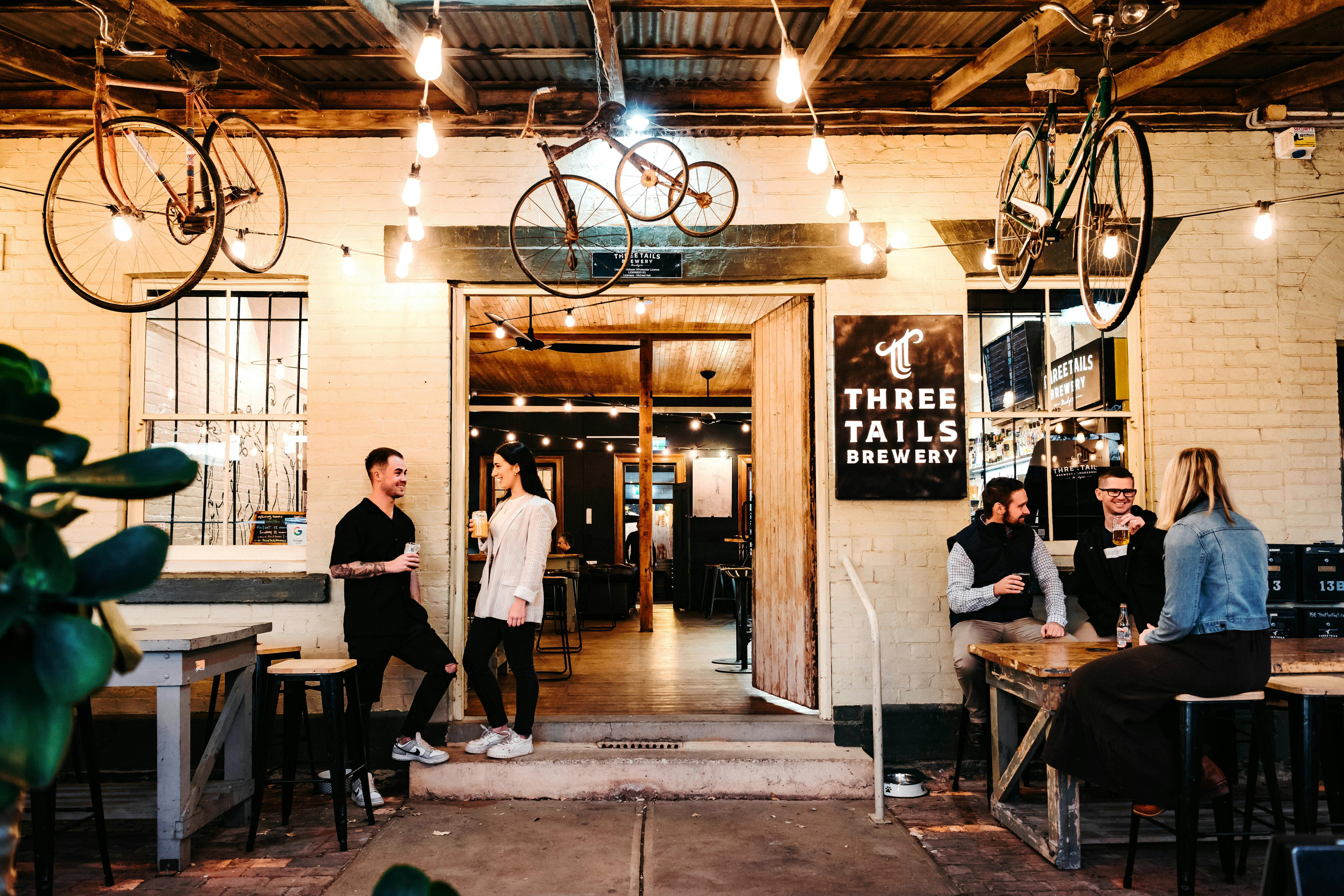 スリー・テイルズ・ブルワリーの正面玄関、天井から吊り下げられた自転車、会話する人々