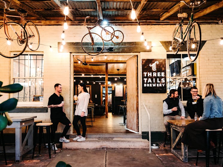 The front entrance to Three Tails Brewery, bikes hanging from ceiling, people conversing