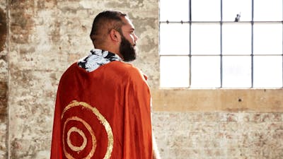 A man stand away from camera with a red cape and gold circles painted on it
