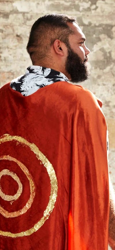 A man stand away from camera with a red cape and gold circles painted on it