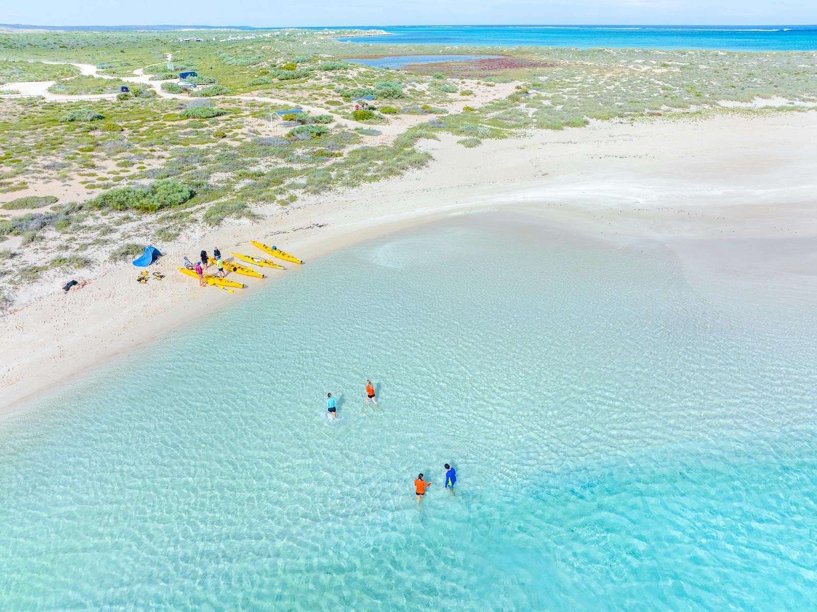 Aerial view of four people relax in Turquoise water with kayaks on a white sandy beach