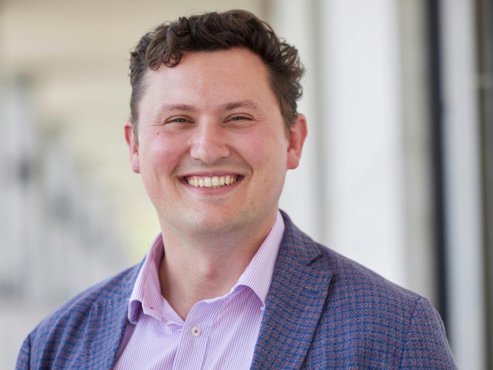 A man wearing a button down shirt and blue blazer while smiling at the camera