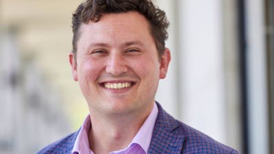 A man wearing a button down shirt and blue blazer while smiling at the camera