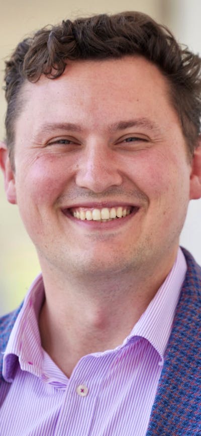 A man wearing a button down shirt and blue blazer while smiling at the camera