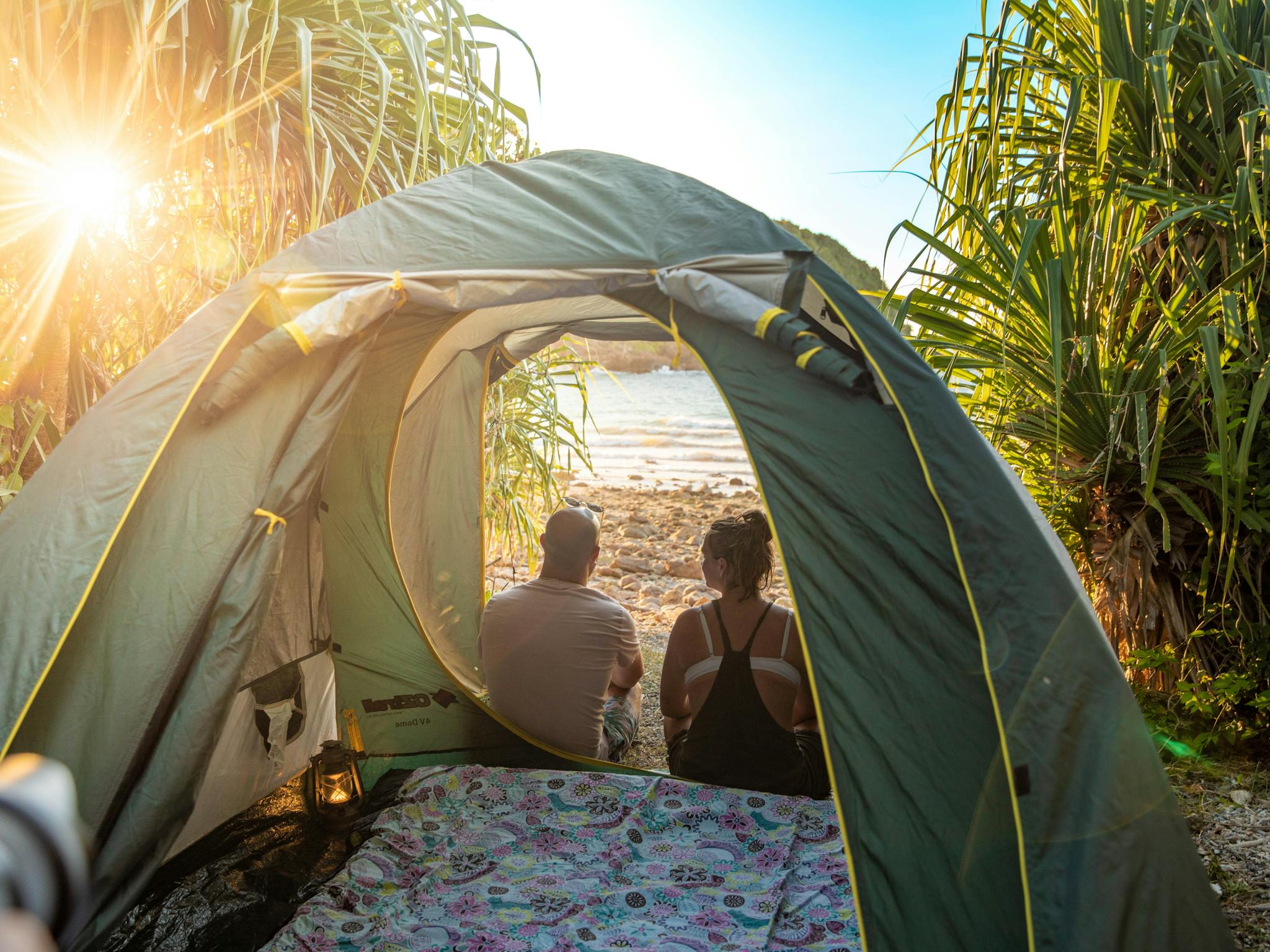 A caucasian couple watches sunset from their tent on a tropical island A caucasian couple watches sunset from their tent on a tropical island