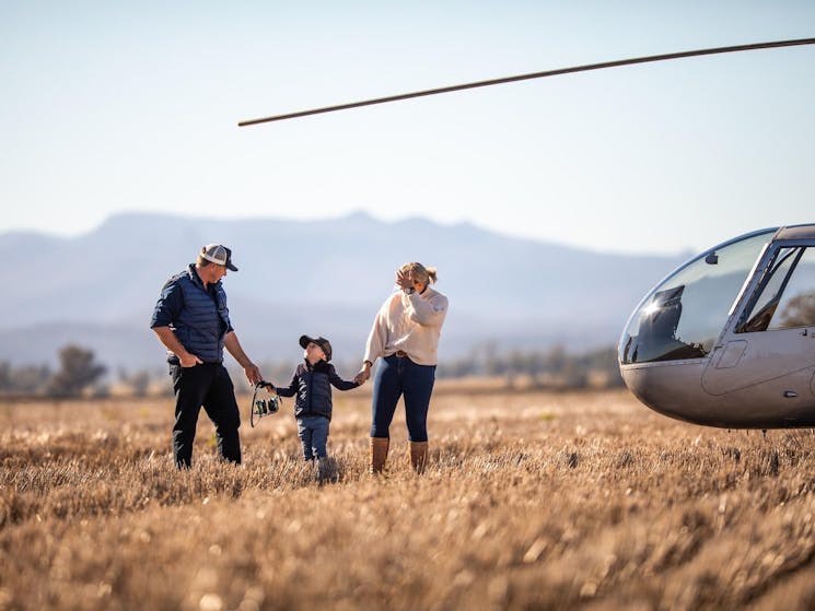 Bryce the pilot stands in a paddock with child and child's mother with Helicopter in the foreground