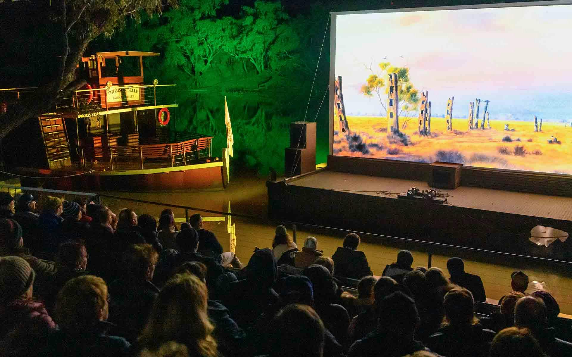 Audience watching a big screen on the riverbank